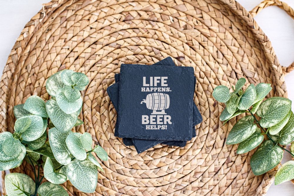 Dark blue coaster with 'Life and Beer' text displayed on round woven placemat with green leaf decoration.