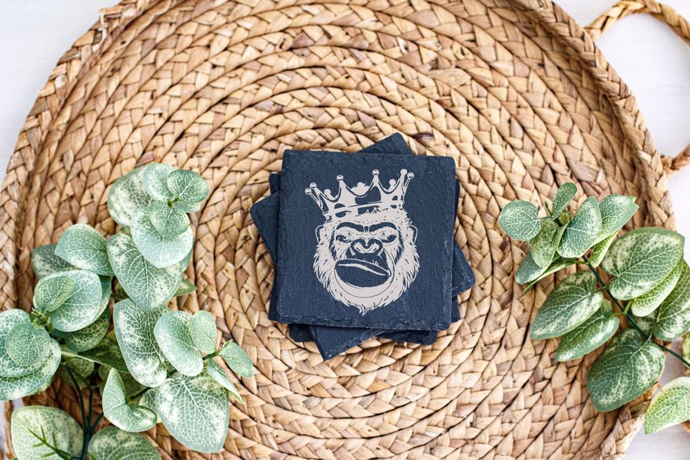 Decorative navy coaster with crown design on circular woven mat accented with artificial green foliage.
