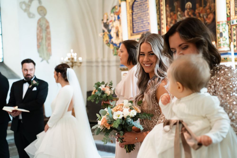 Wedding ceremony in a historic church with bridesmaids holding floral bouquets.