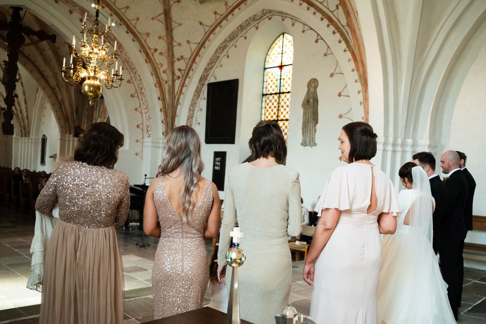 Back view of wedding party in elegant dresses standing in ornate church during ceremony.