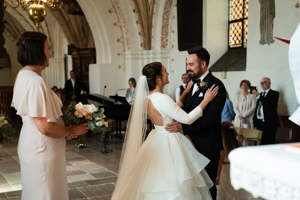 A couple embraces during their wedding ceremony as an officiant stands nearby in a beautiful church interior.