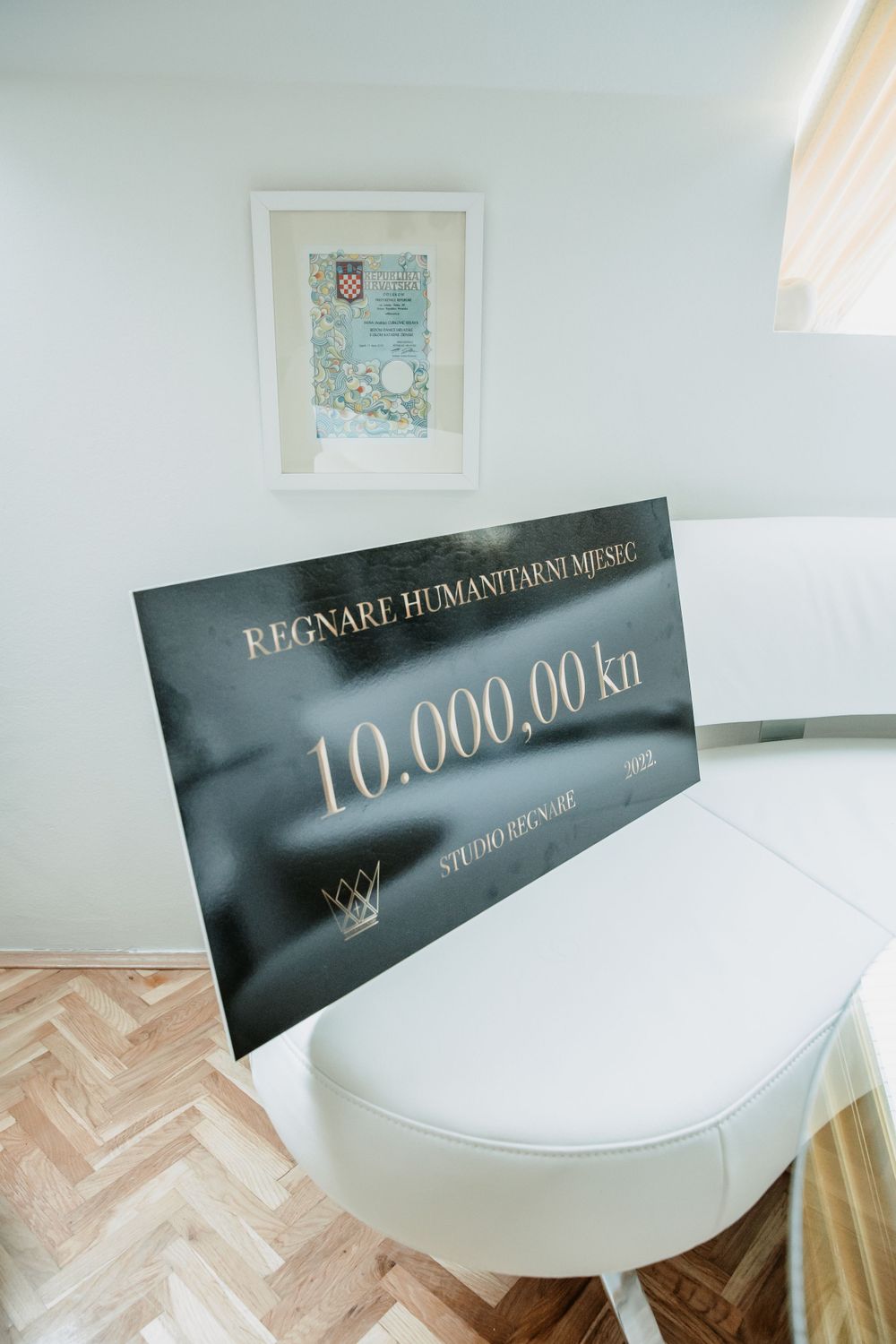 Large black check or gift card showing 10,000.00 kr value displayed on white furniture with framed artwork.