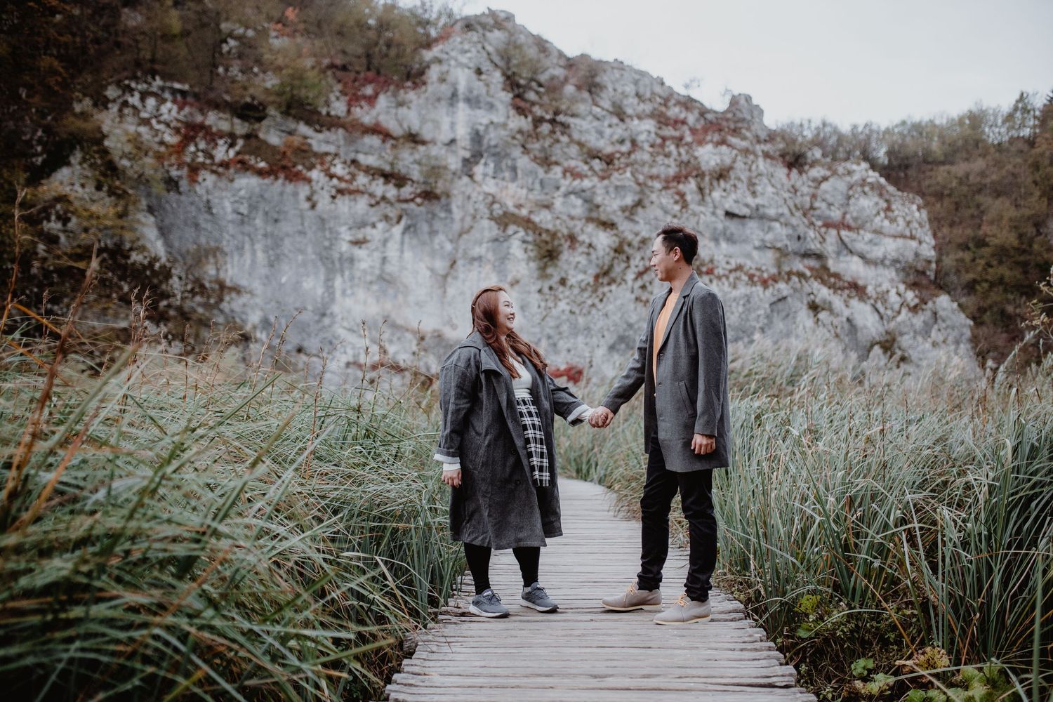 A couple poses playfully against a rustic fence with autumn mountains in the background.