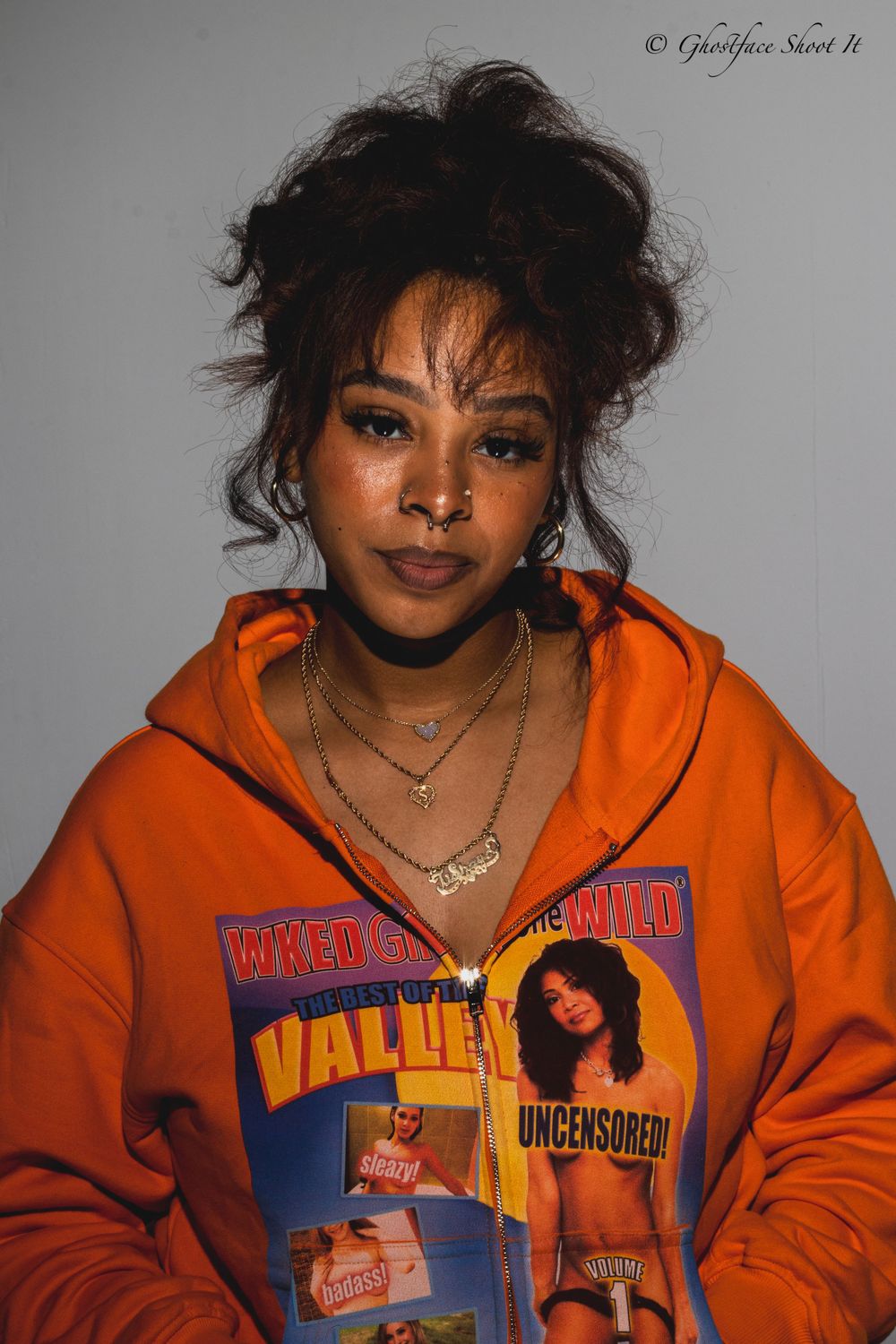 Close-up portrait in orange hoodie with layered necklaces and vintage graphic design.