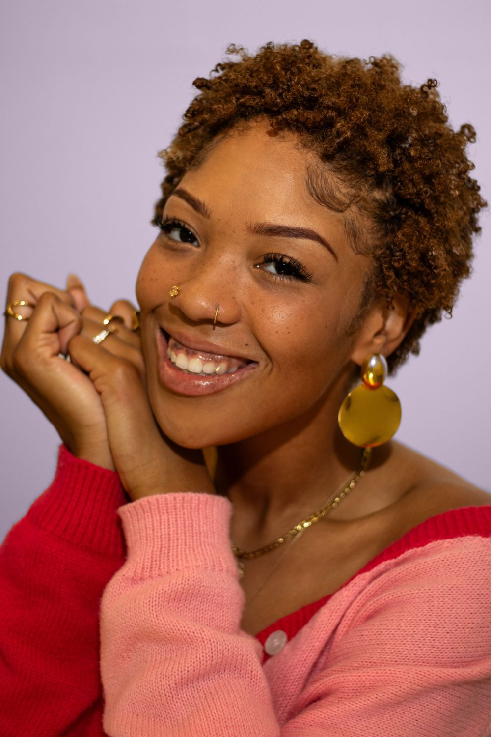 Portrait of person wearing pink sweater and gold earrings with natural curly hair.