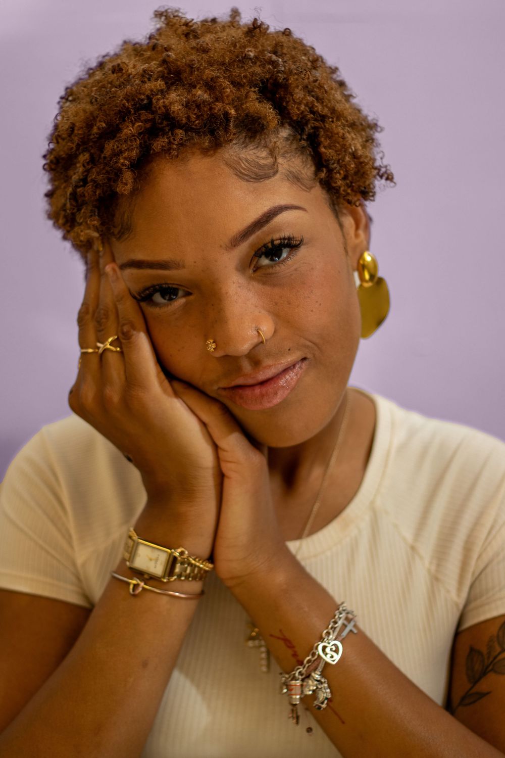 Warm casual portrait with golden jewelry and white t-shirt against soft purple backdrop.