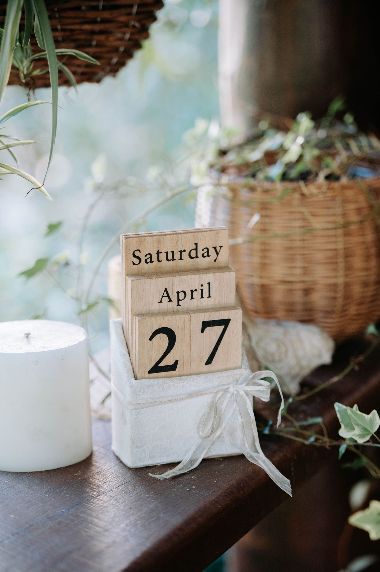 A wooden calendar block displaying Saturday April 27 sits next to a white candle and potted plants.