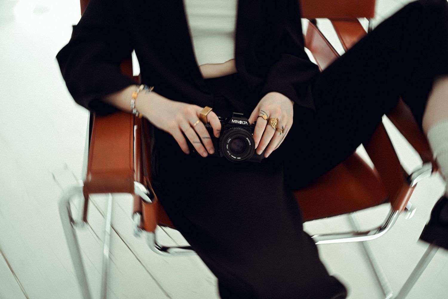 Close-up shot of hands holding a vintage camera while seated in a white chair.