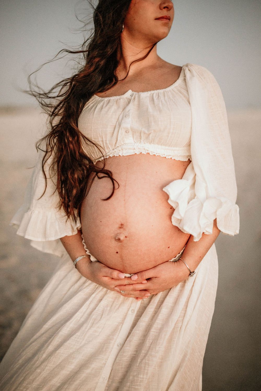 Side view of pregnant belly with white cropped top and flowing skirt.
