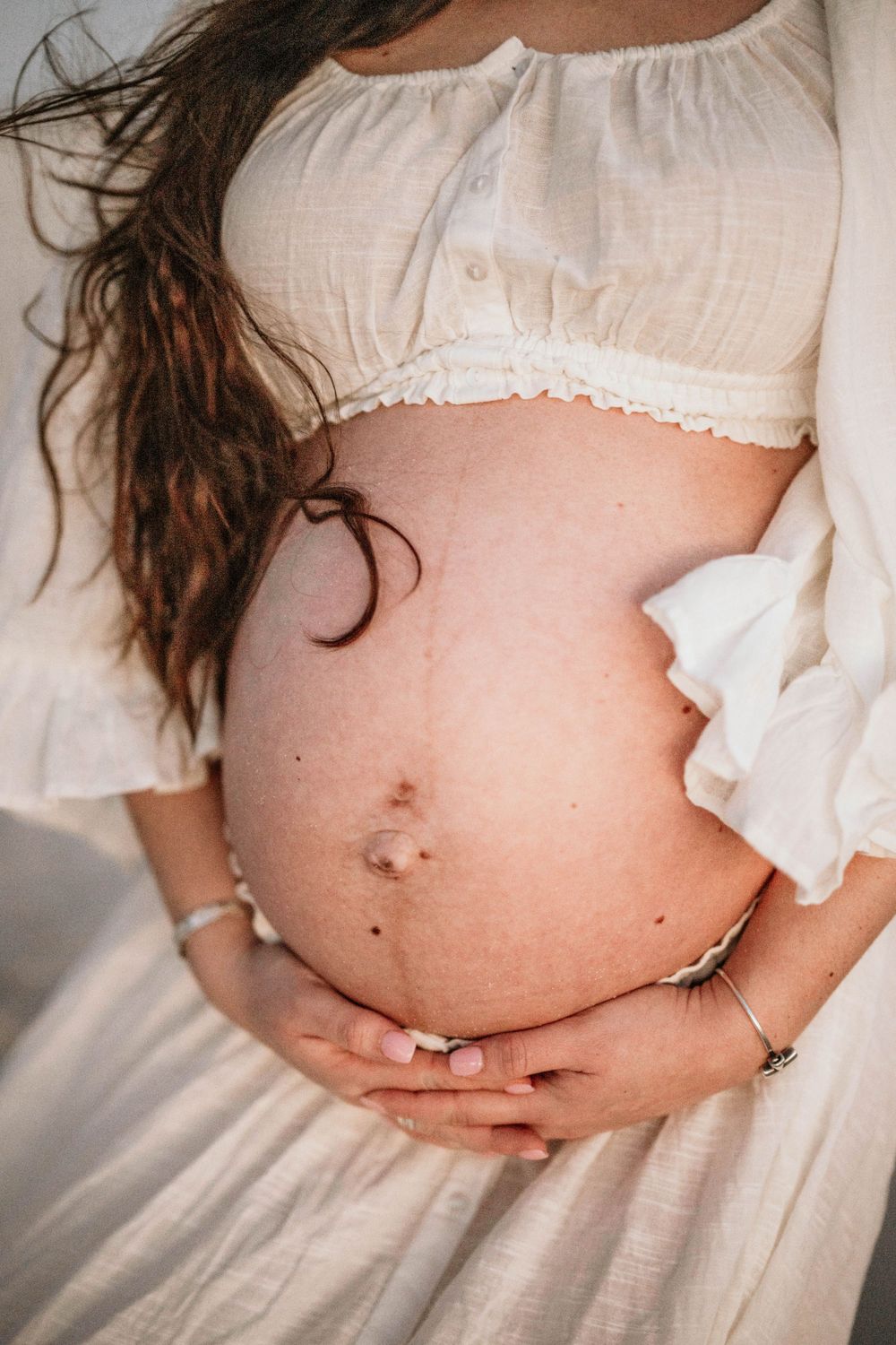 Close-up maternity photo showing a bare pregnant belly with white ruffled clothing.