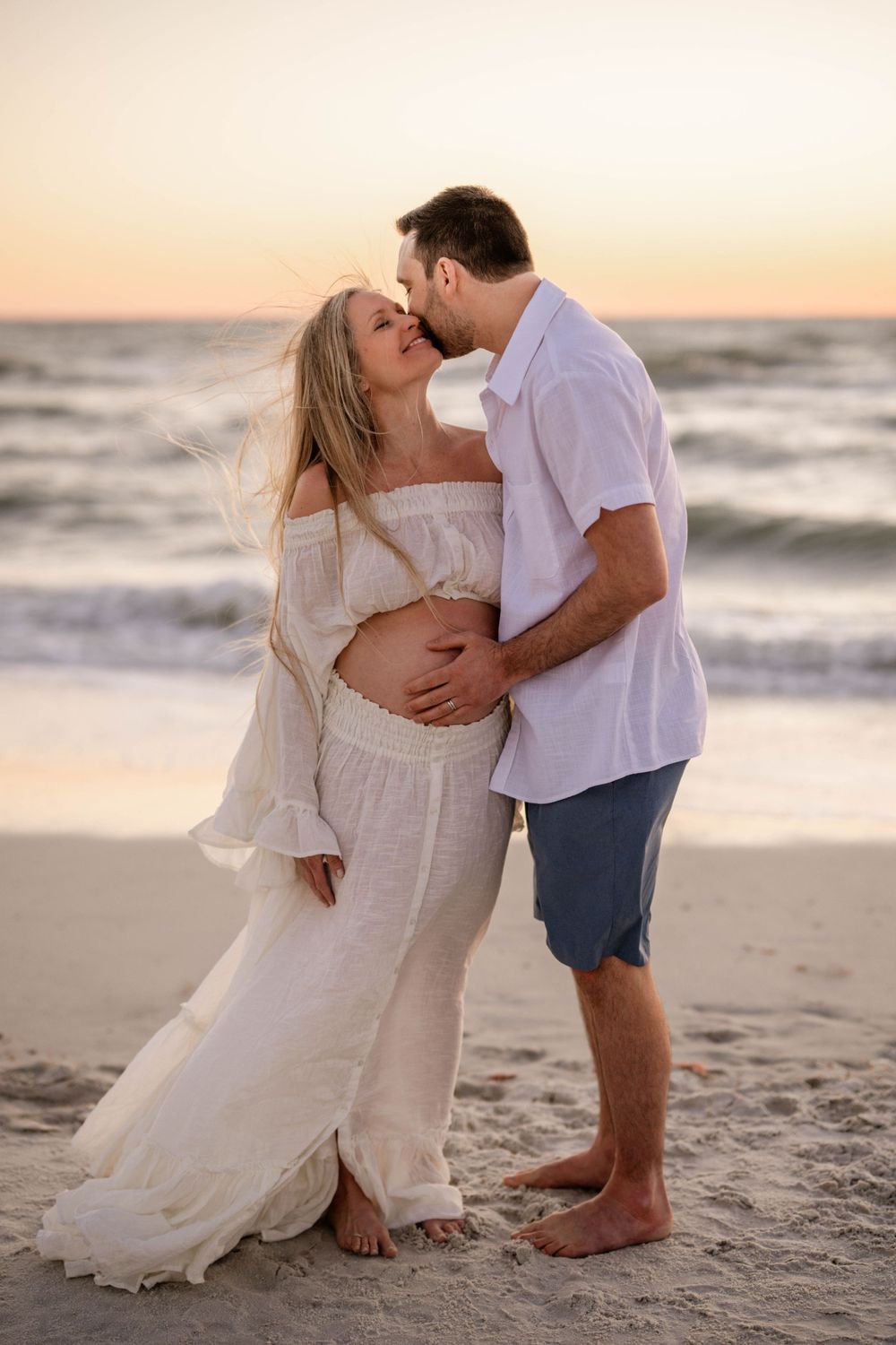 A tender embrace captured on the beach at sunset with waves in the background.