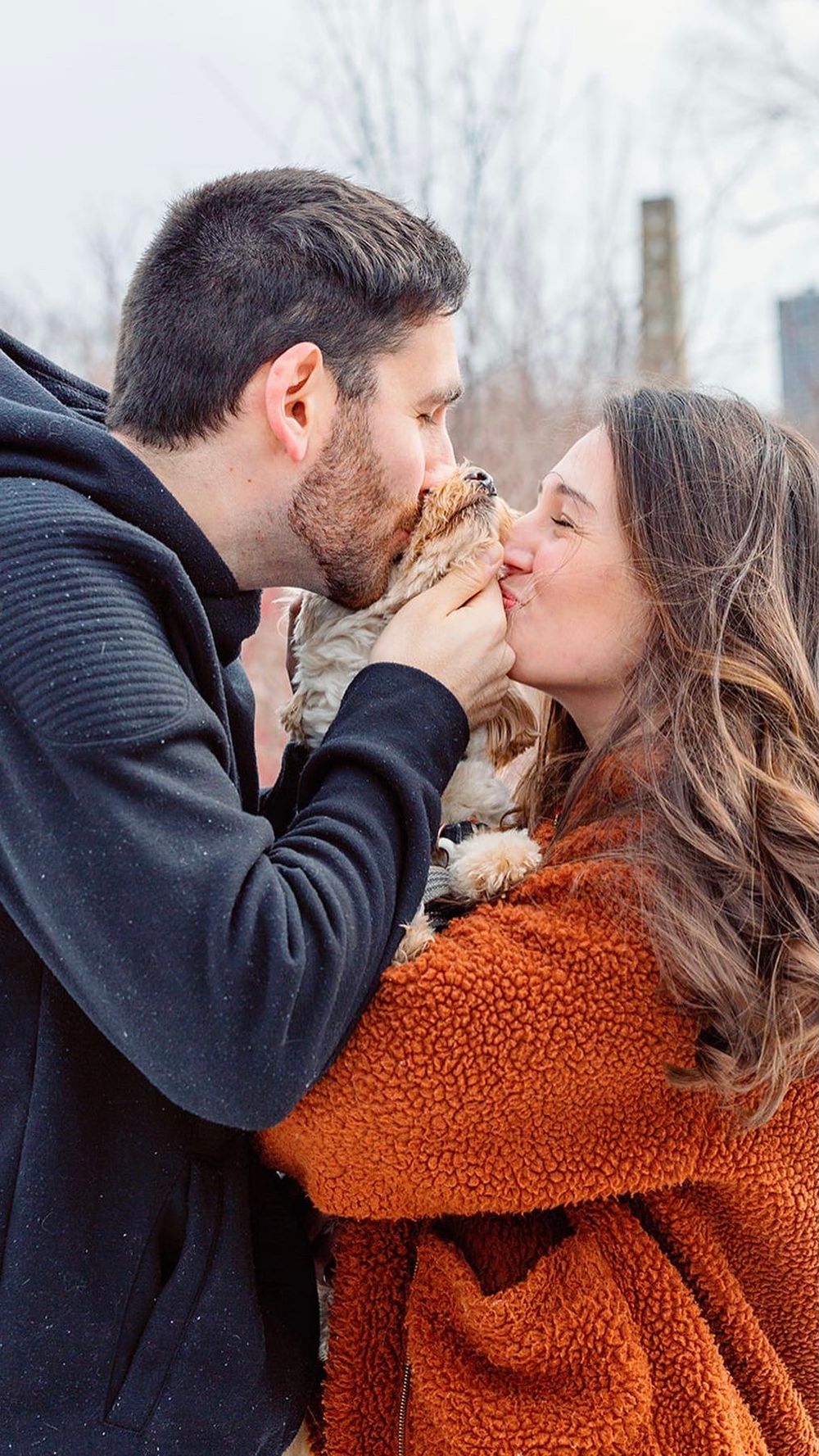 Couple sharing intimate kisses in winter scene wearing black coat and orange sweater.