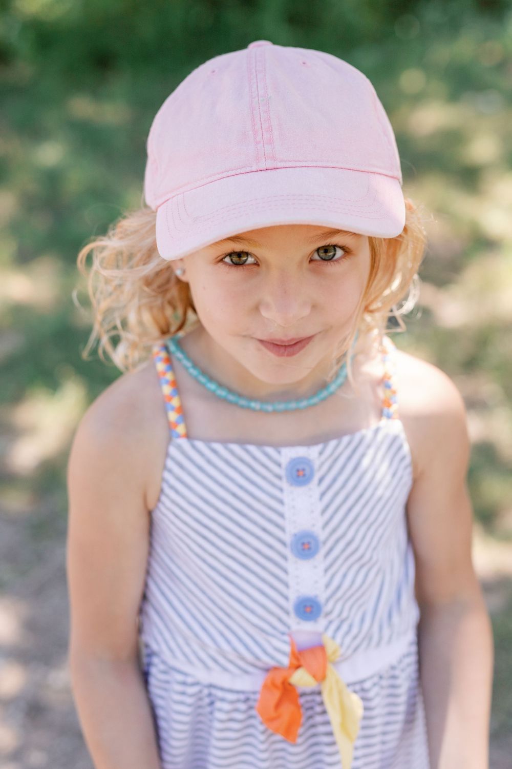 Close-up portrait series of someone wearing a striped dress and pink cap in summer light.
