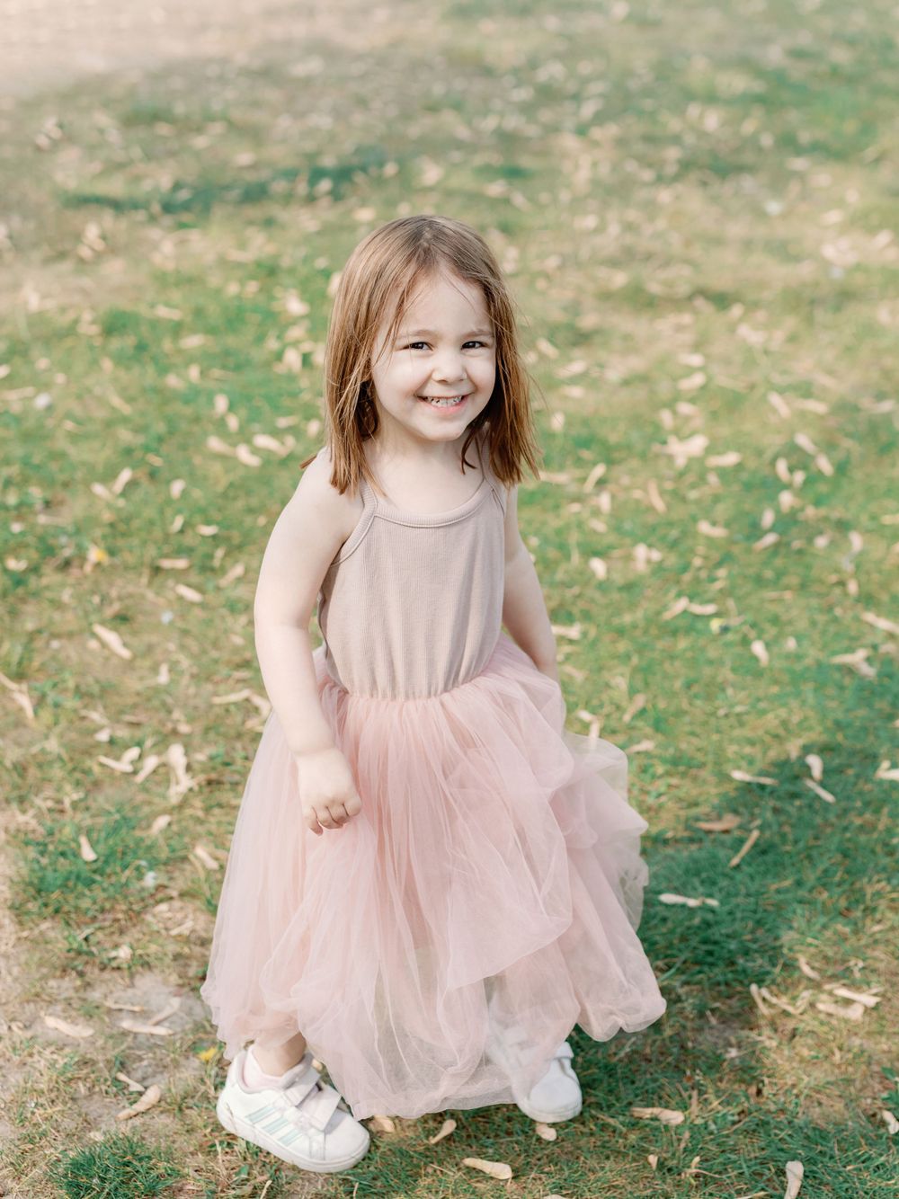 Young child twirls in pink tulle dress on grassy lawn.