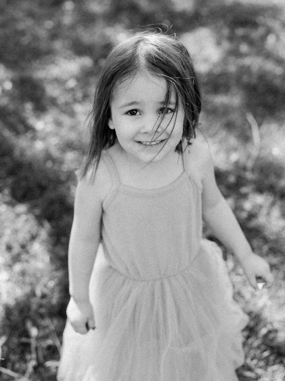 Black and white portrait of child in sleeveless dress outdoors.
