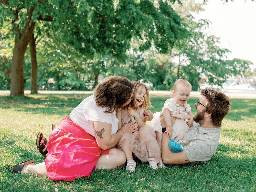 Family relaxing together on grass under shady trees in park.
