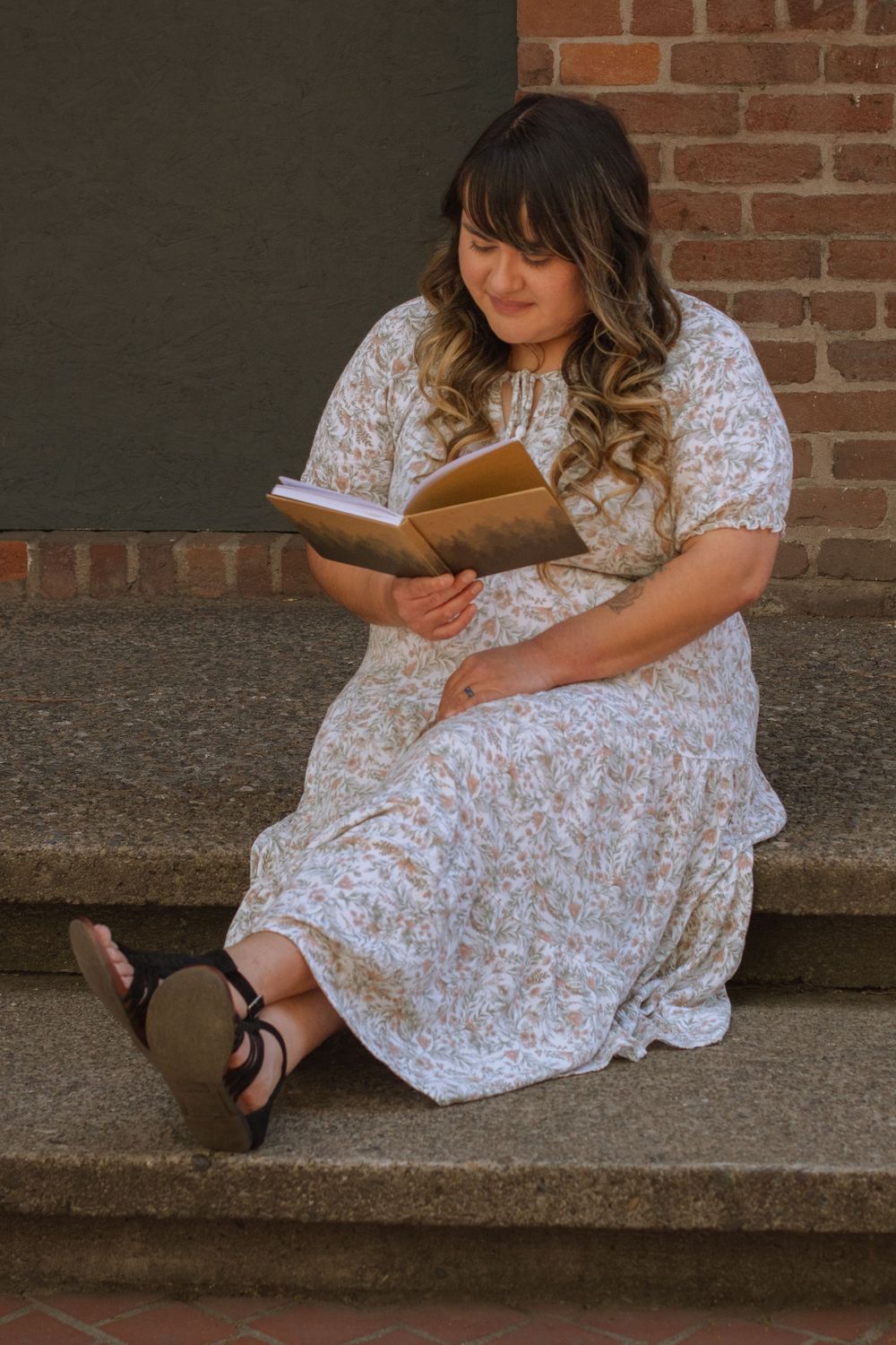 Woman sitting on stairs working in journal in front of brick wall.