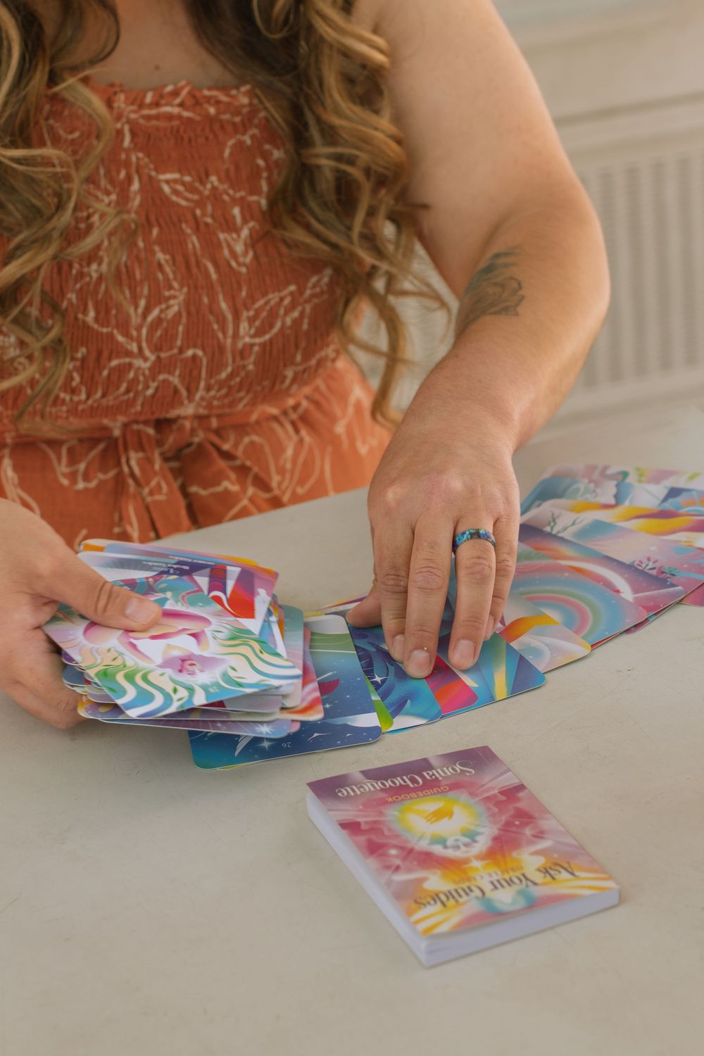 Close up view of woman wearing an orange floral jumpsuit dealing multicolored tarot card deck.