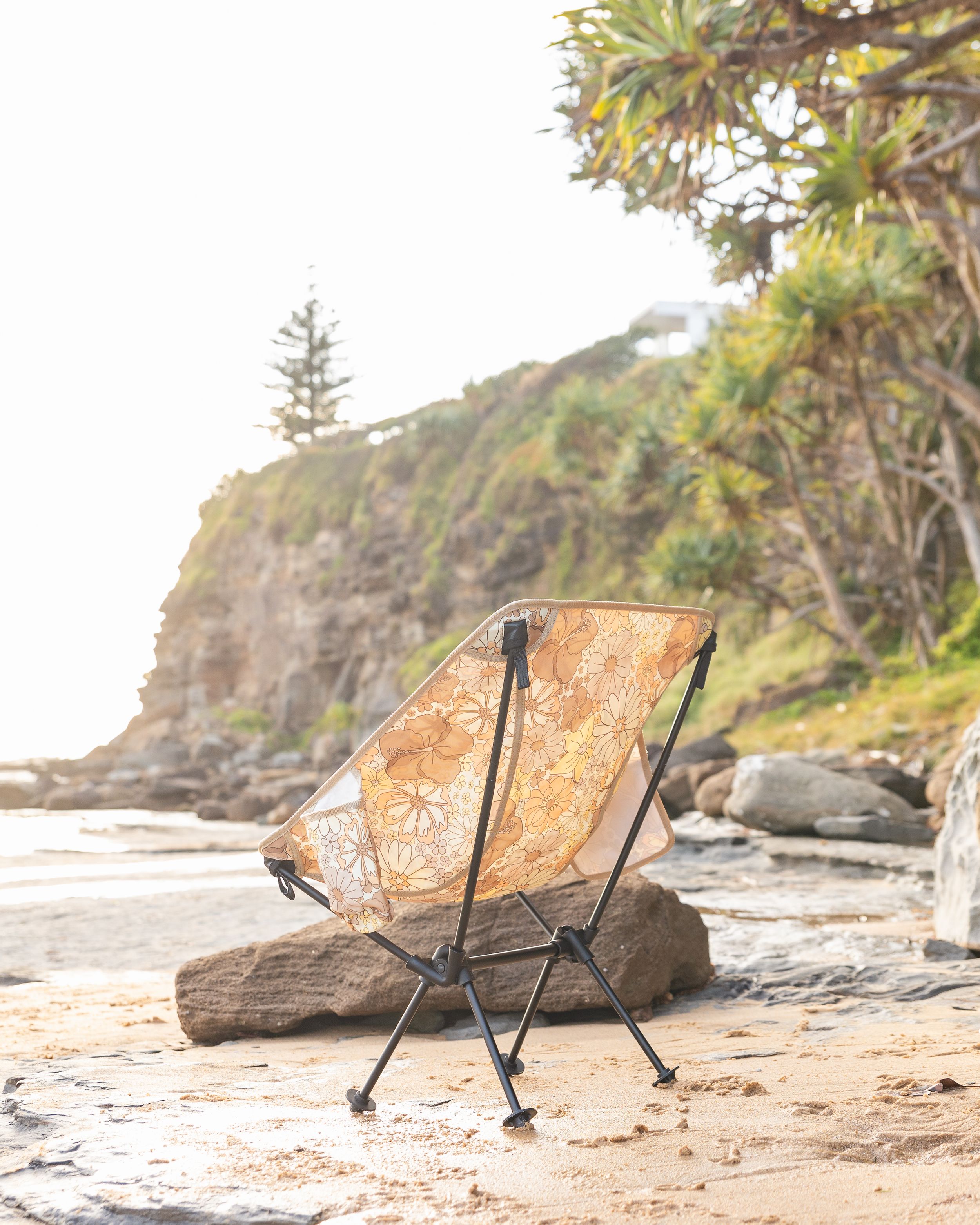Beach chairs positioned on rocky shore with coastal cliffs in background. Campout Co Camping Chairs Product Photography.