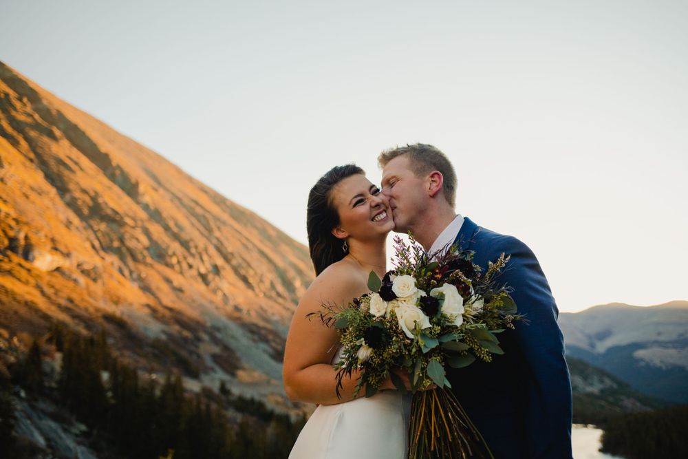 A romantic sunset wedding portrait with a bouquet of white flowers against mountain backdrop.