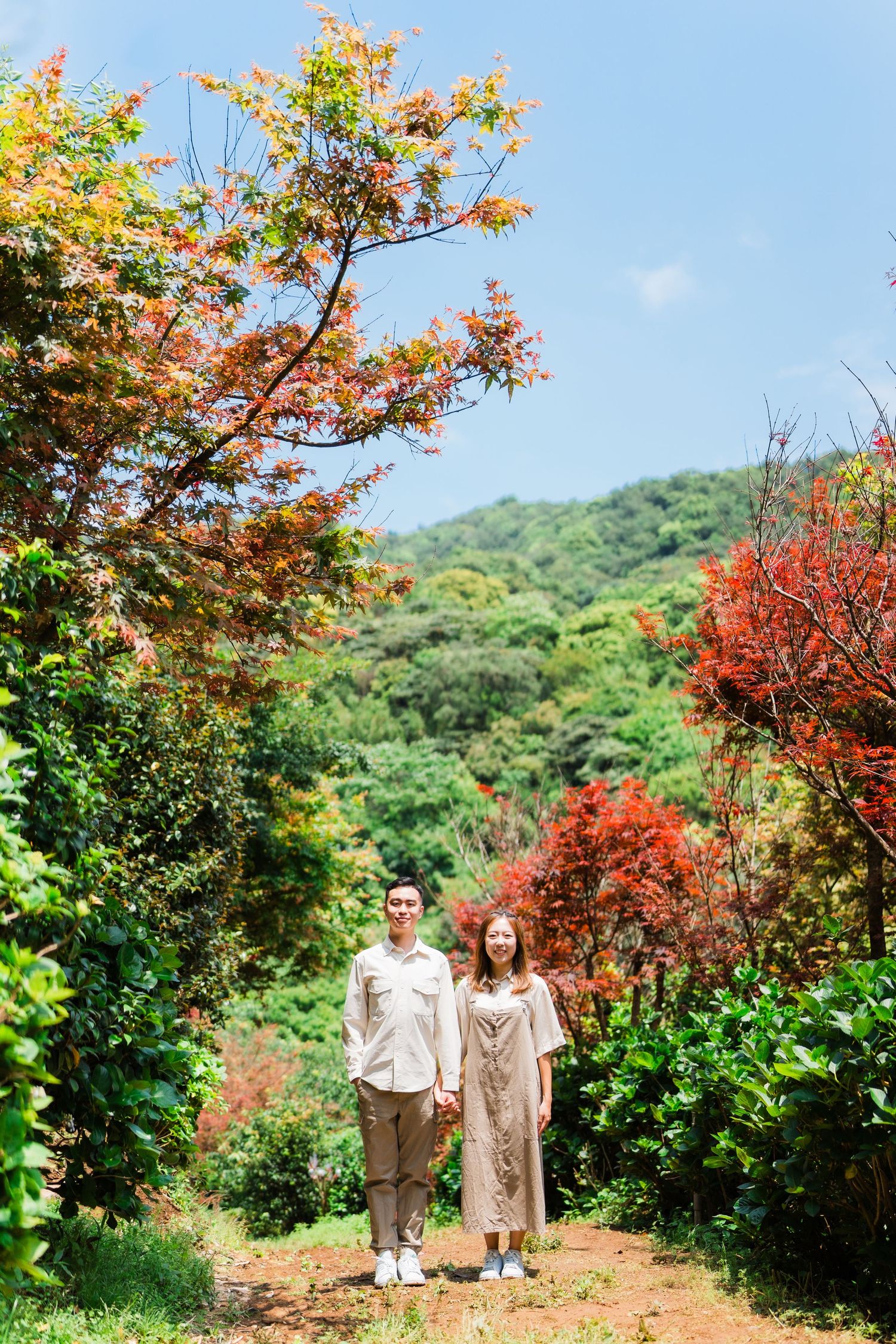Two people stand on a path surrounded by vibrant autumn foliage and greenery.