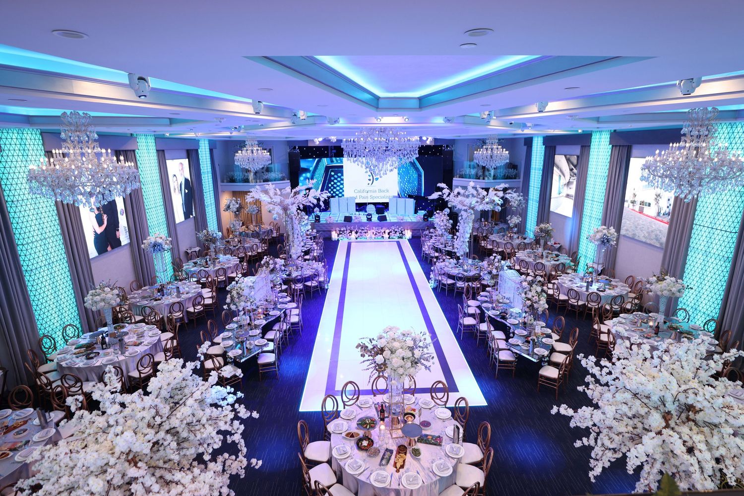 Modern wedding reception ballroom with blue lighting, white decor, and illuminated runway-style aisle.