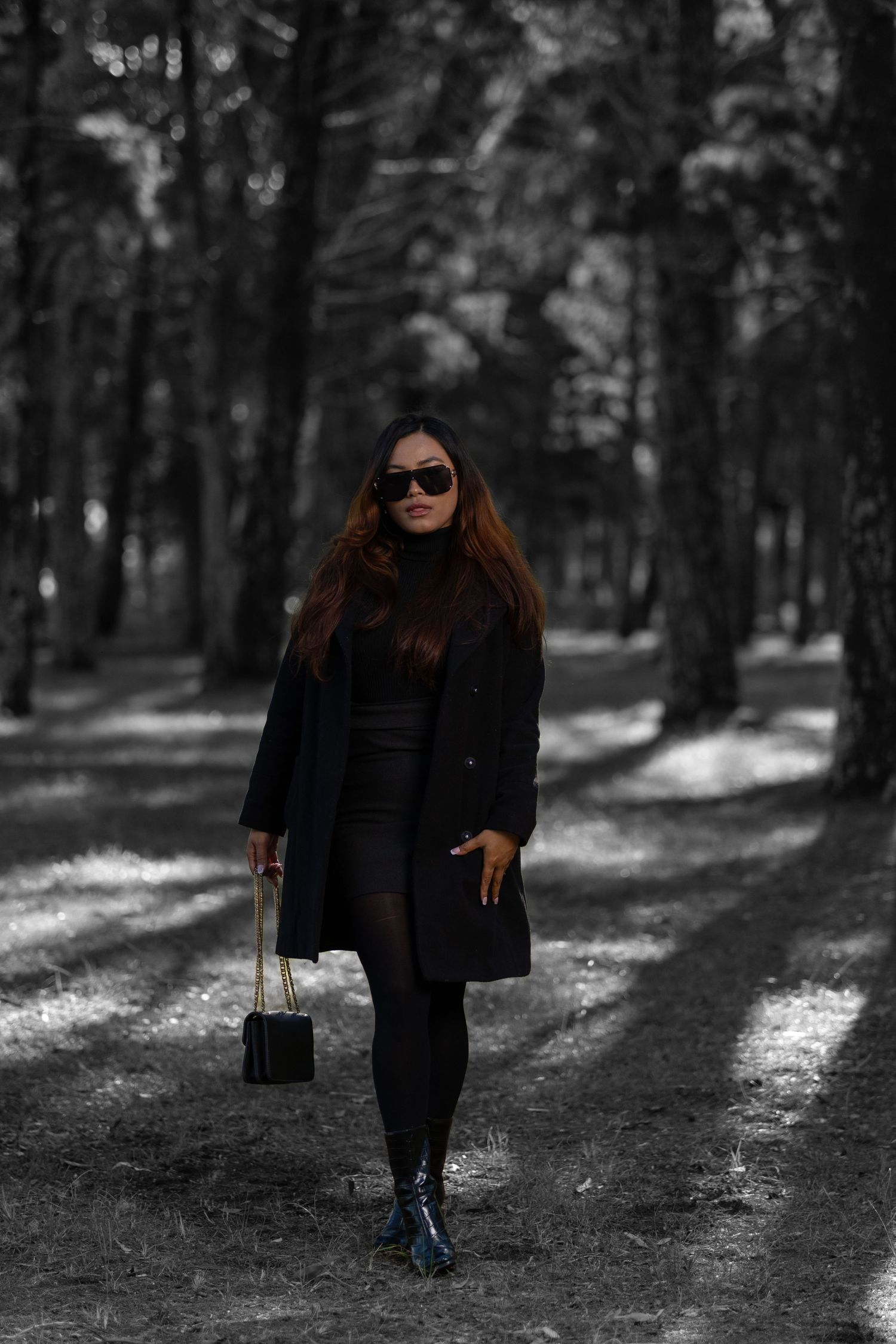 Stylish winter fashion portrait in black coat and sunglasses walking through a forest path.