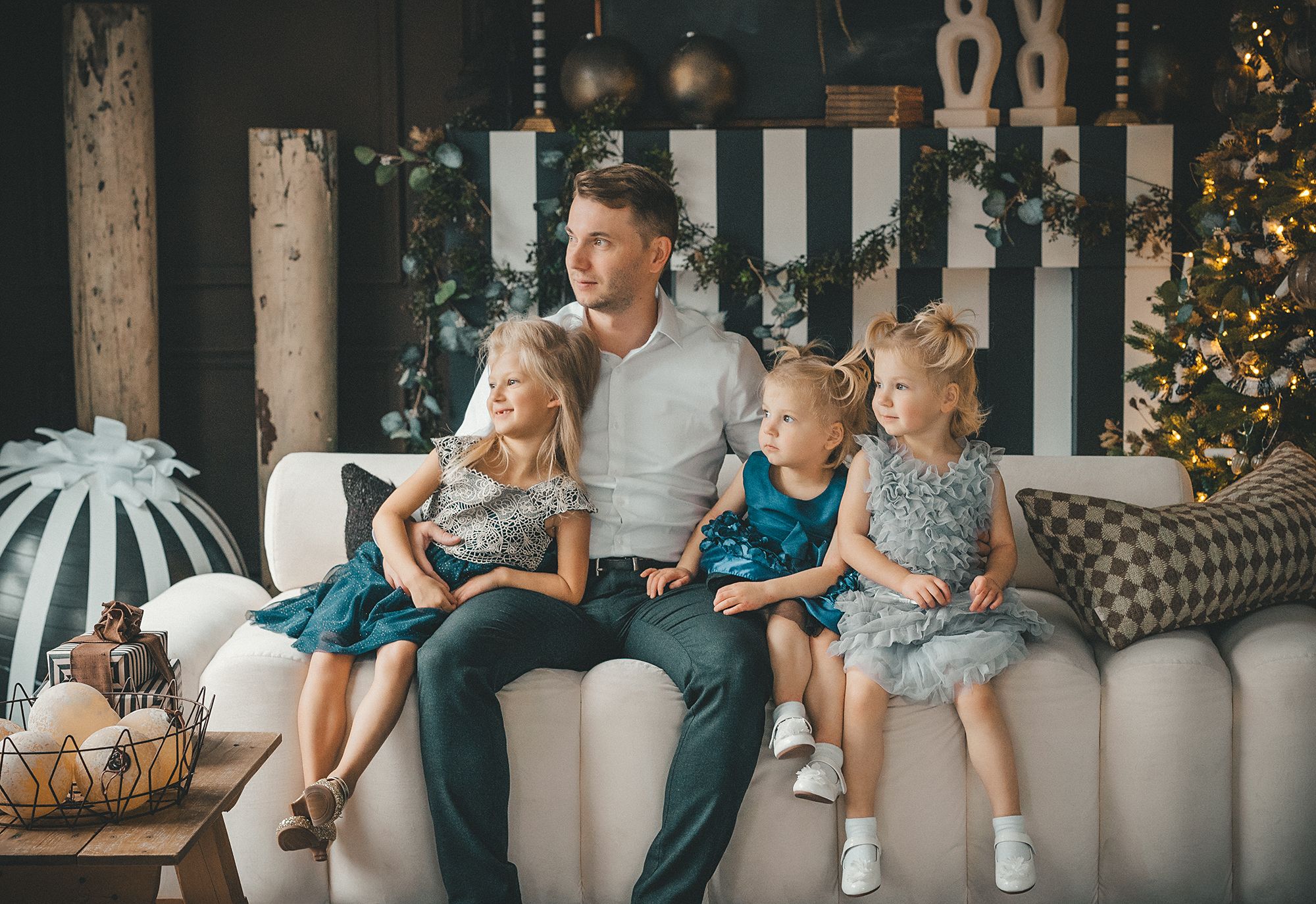 a dad with three daughters are posing on the couch during the Christmas family photo session at Mint Room studio in