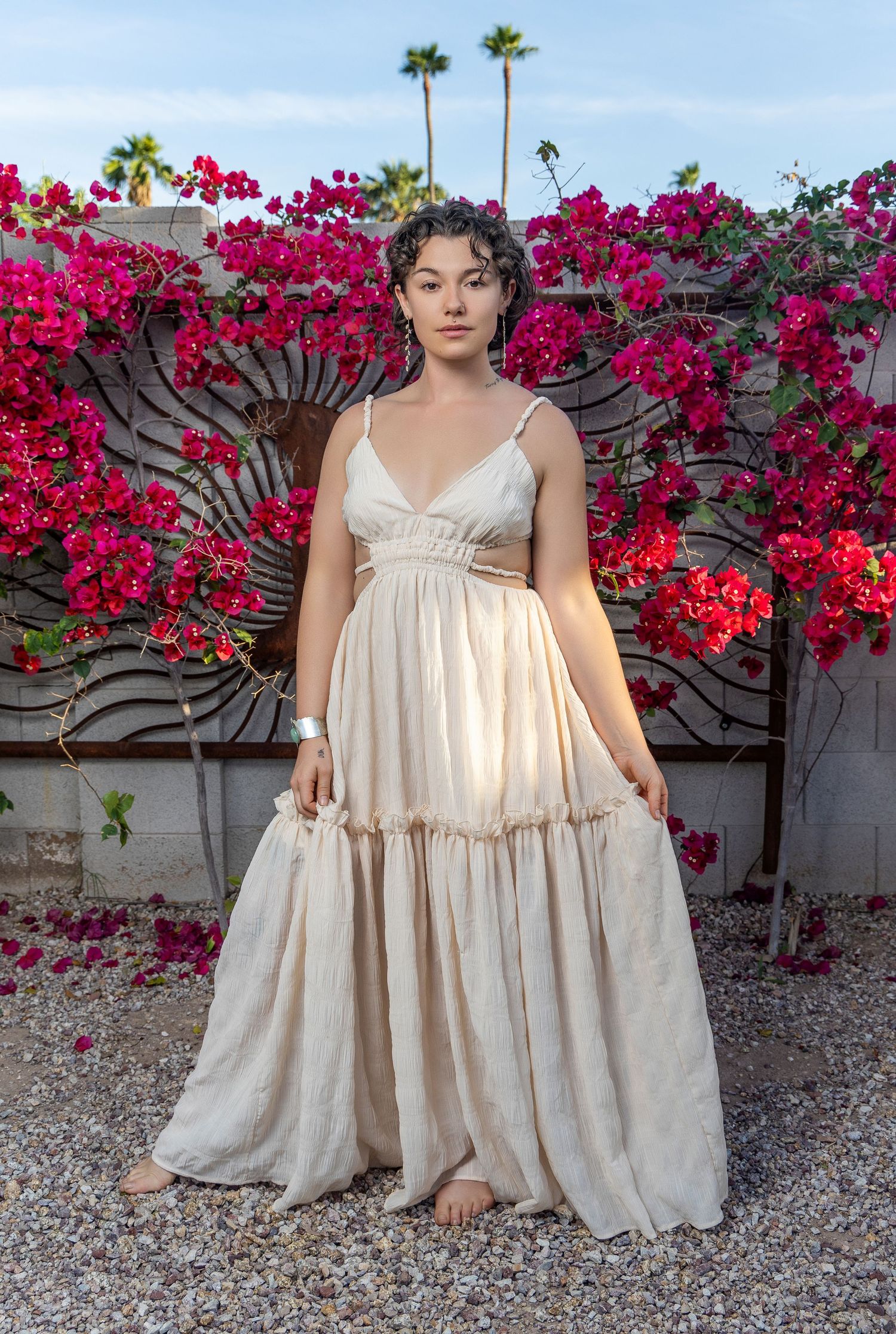Person wearing cream-colored tiered maxi dress poses against wall with vibrant pink bougainvillea flowers.