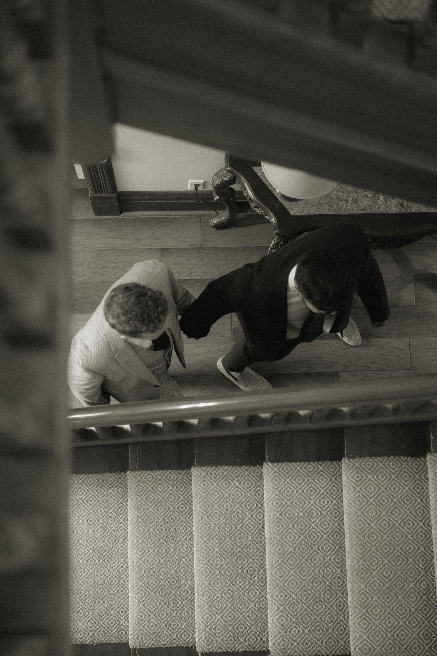 Two people in formal attire lying on carpeted stairs in black and white photography.