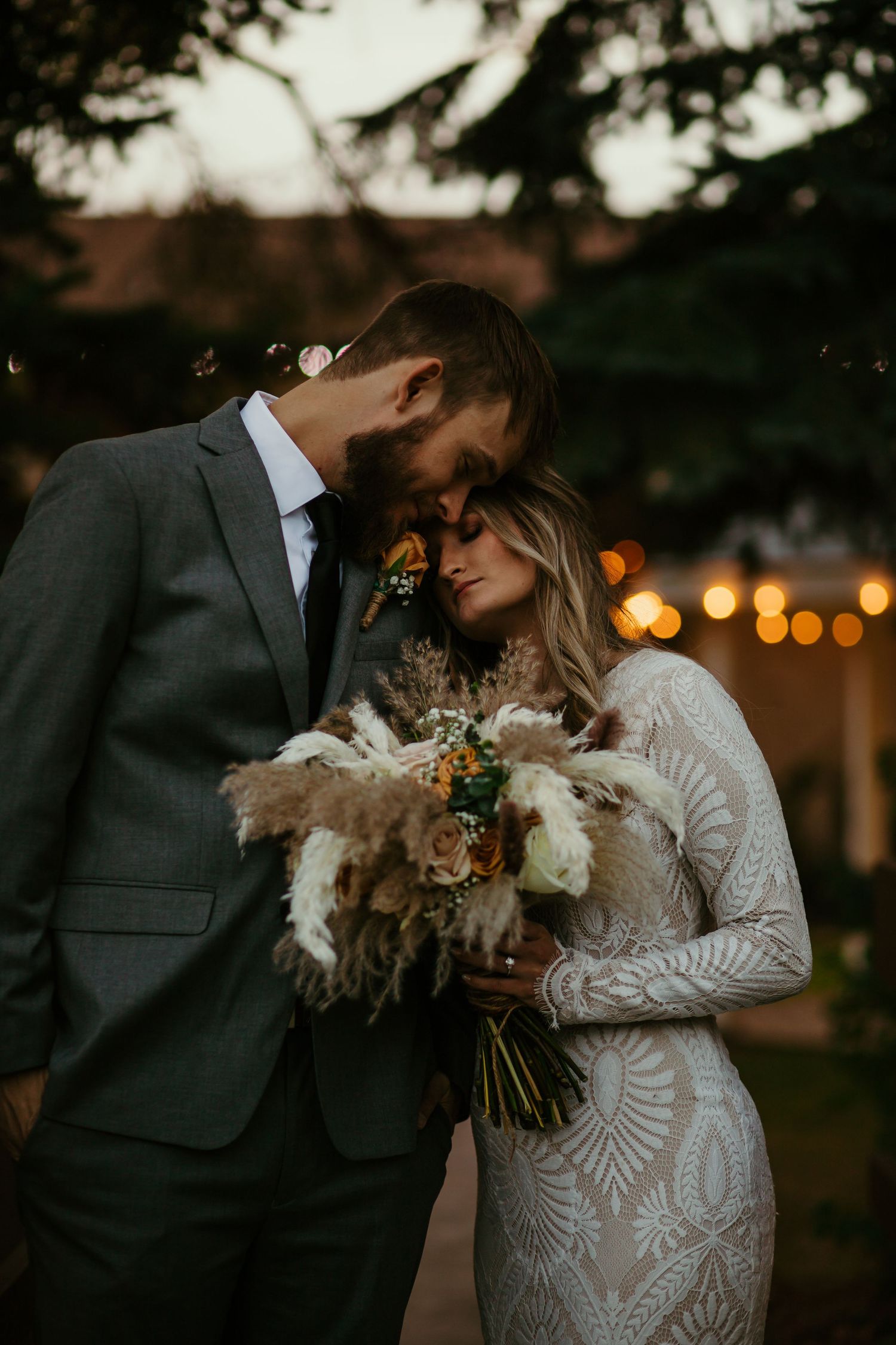 Romantic wedding photo at sunset with a modern bouquet featuring dried flowers and pampas grass.