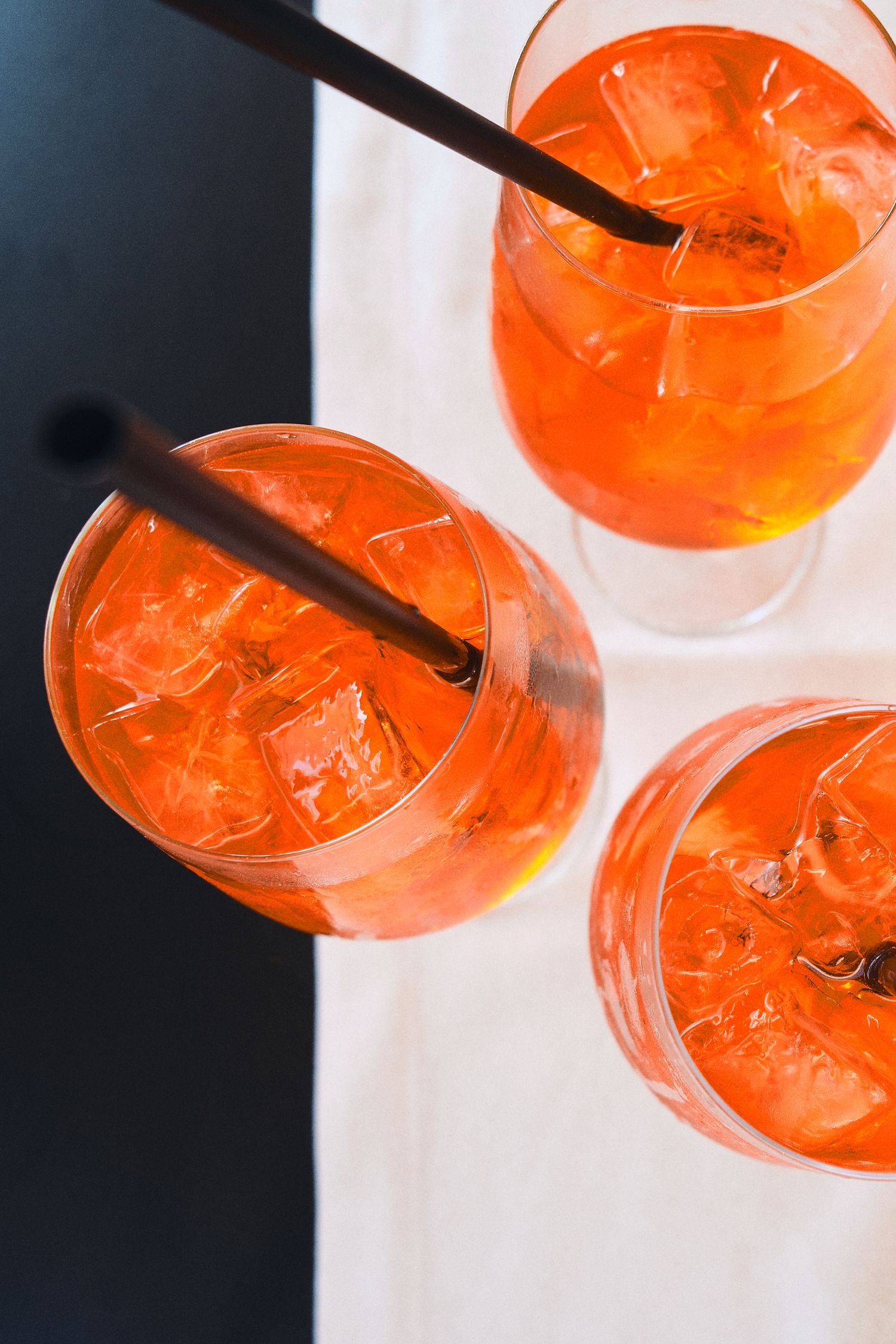 Overhead view of bright orange Aperol Spritz cocktails with ice and straws.