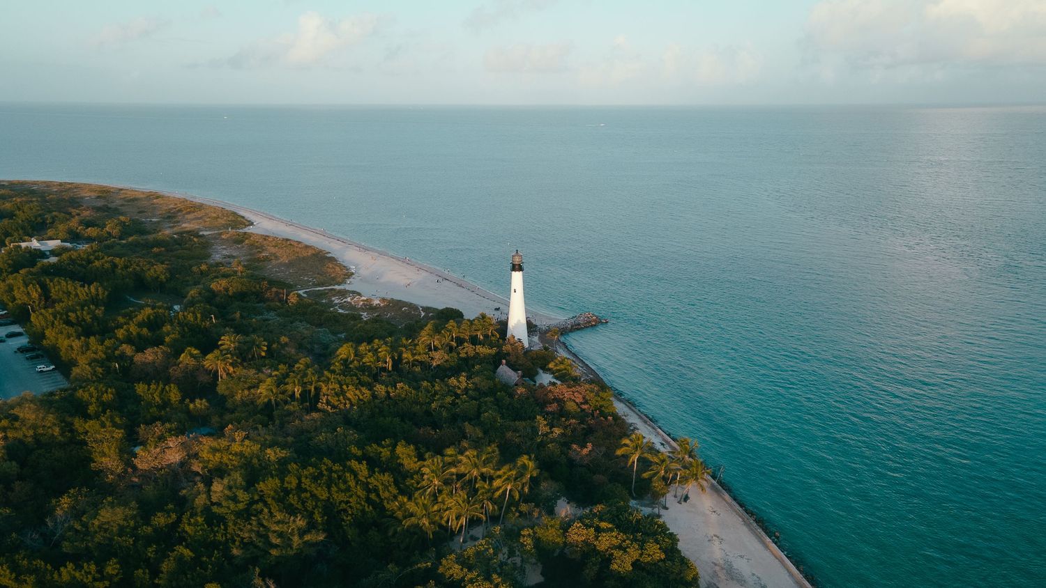 Aerial view of white lighthouse on coastal peninsula surrounded by turquoise waters.