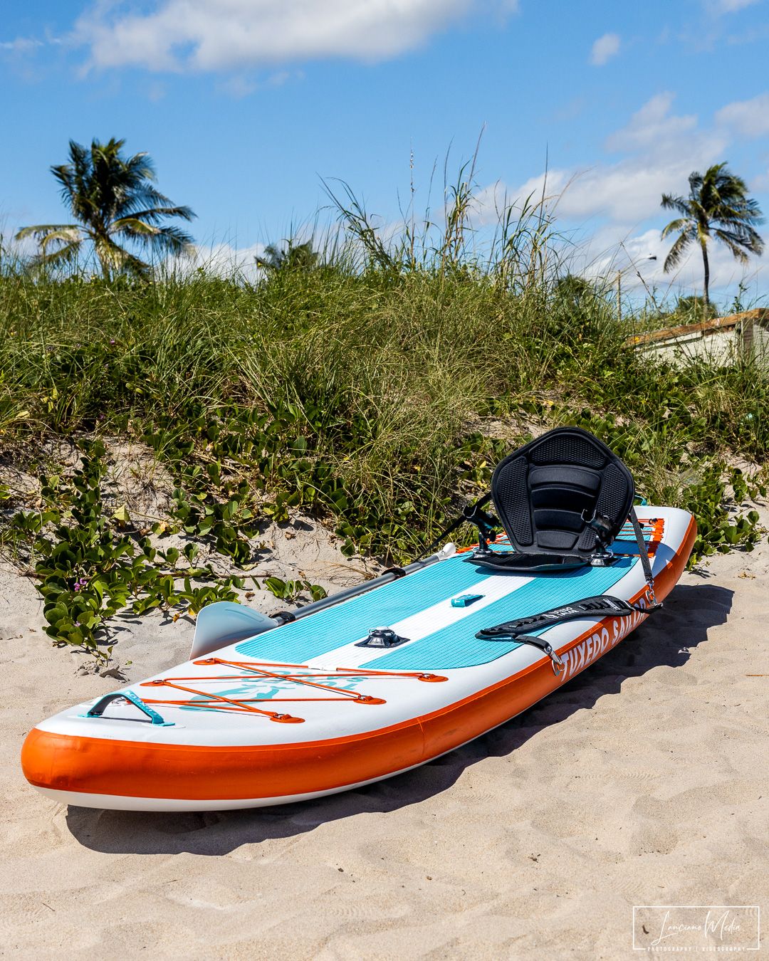 Colorful paddleboard with blue and orange design lying on sandy beach with palm trees in background.