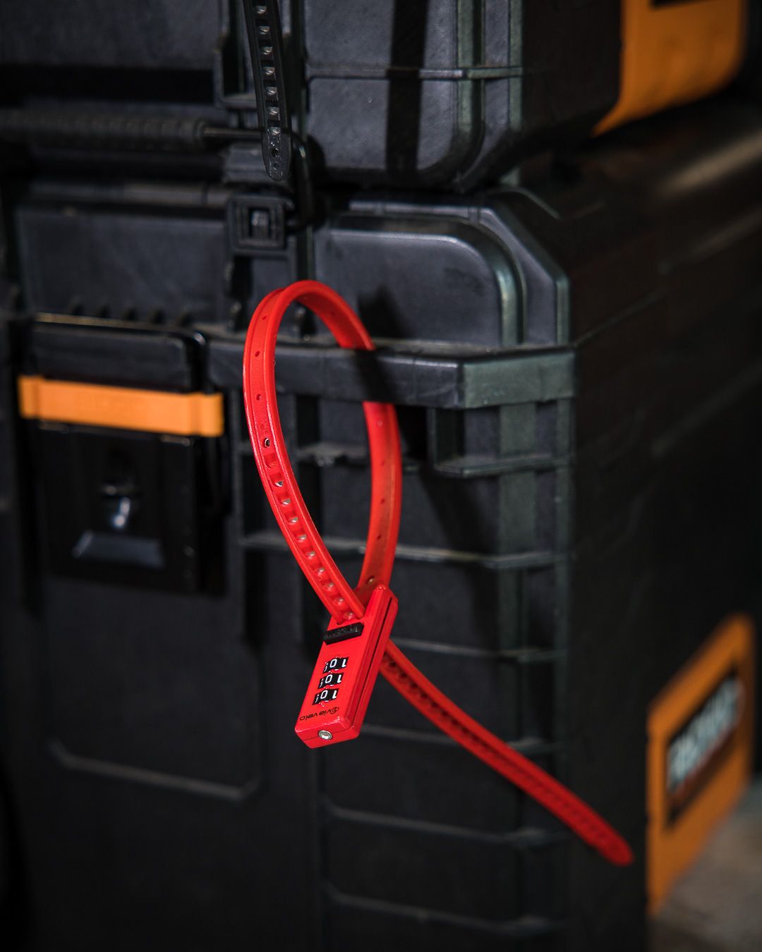 Red security zip tie attached to black industrial storage case in dark setting.