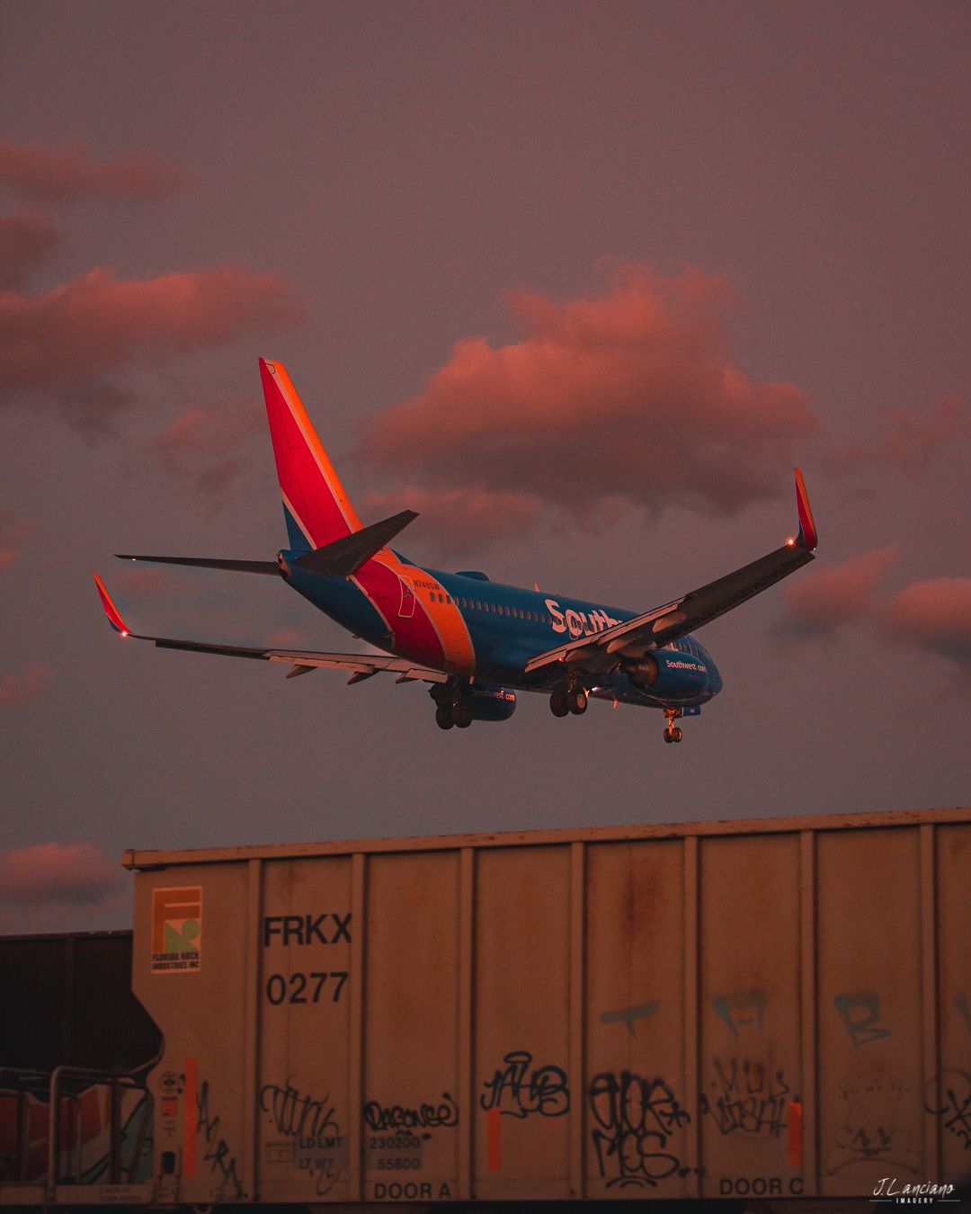 Southwest Airlines plane landing against dramatic red sunset sky above a freight train car.