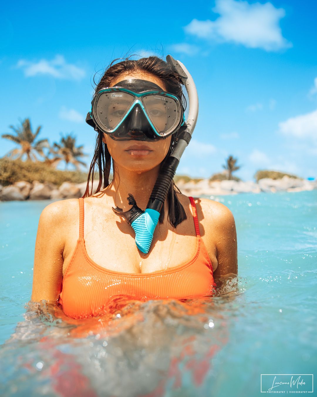Snorkeler in orange swimwear and diving mask floating in tropical blue waters.