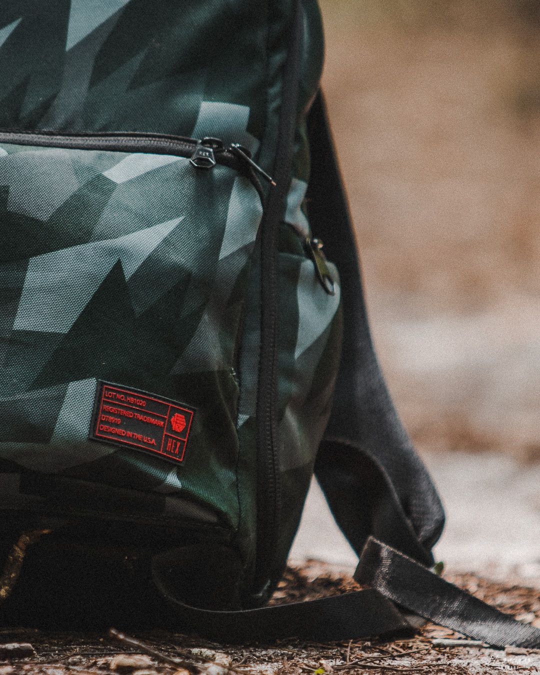Close-up of camouflage backpack zipper pocket with red label detail.