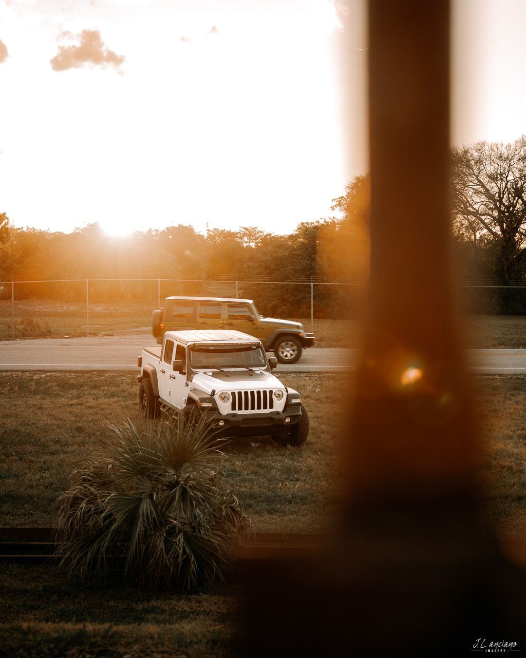 White Jeep photographed through window frame during golden hour sunset.