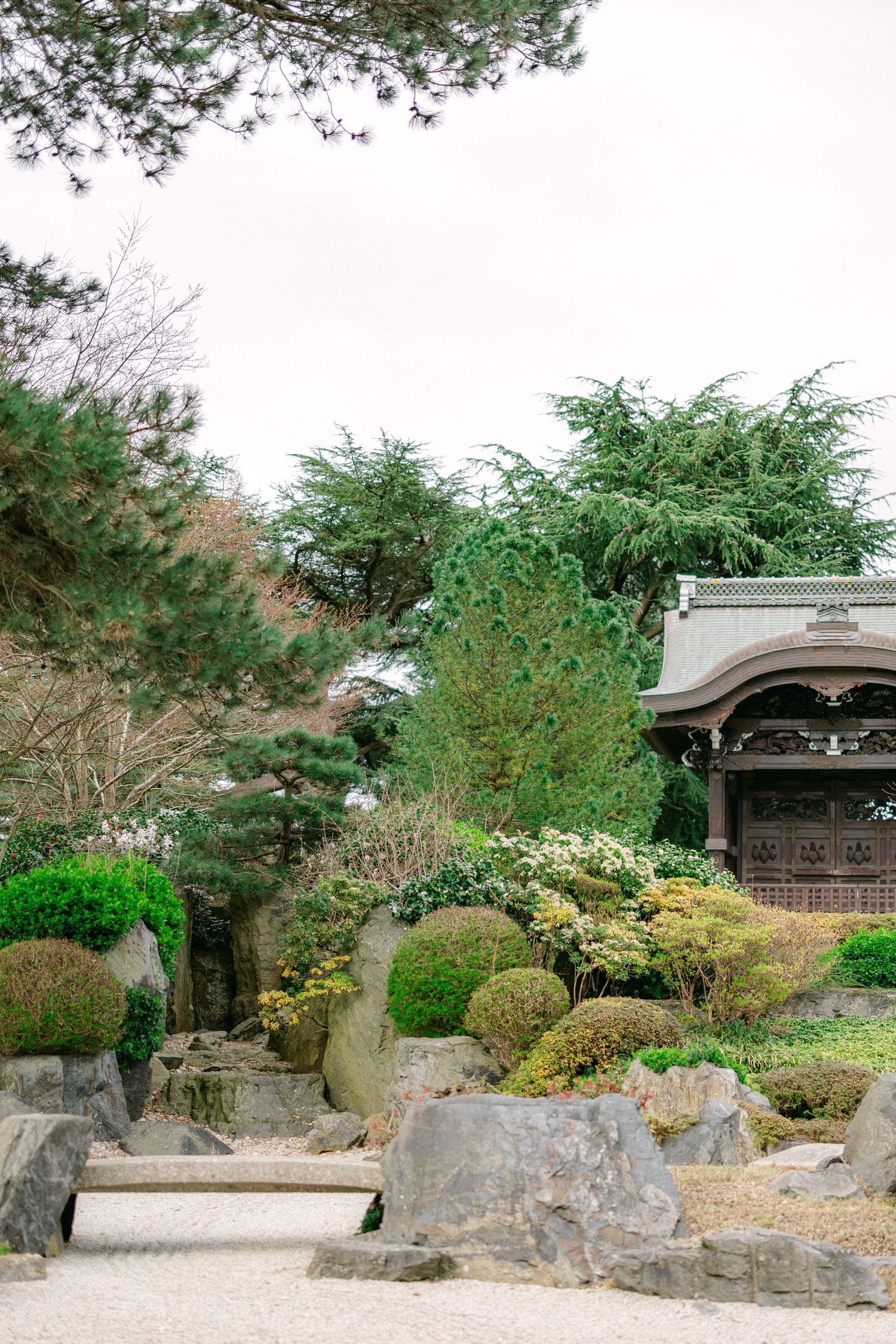 Serene Japanese garden with traditional pavilion, sculpted bushes, and stone pathways.