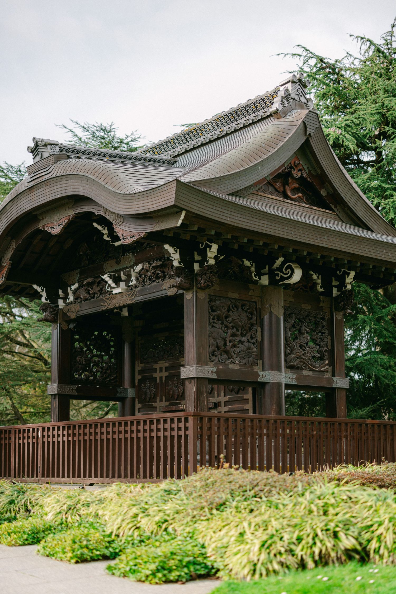 Traditional Japanese pavilion with ornate curved roof and wooden railings surrounded by lush garden foliage.