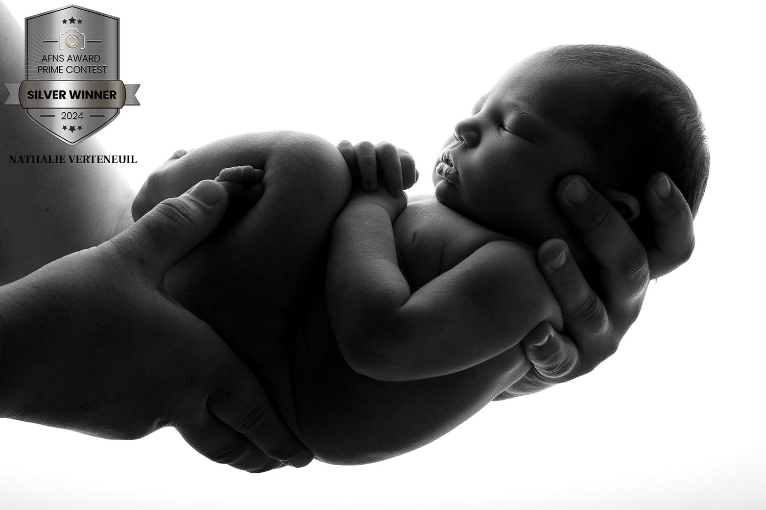 Artistic black and white portrait of a newborn cradled in gentle hands.