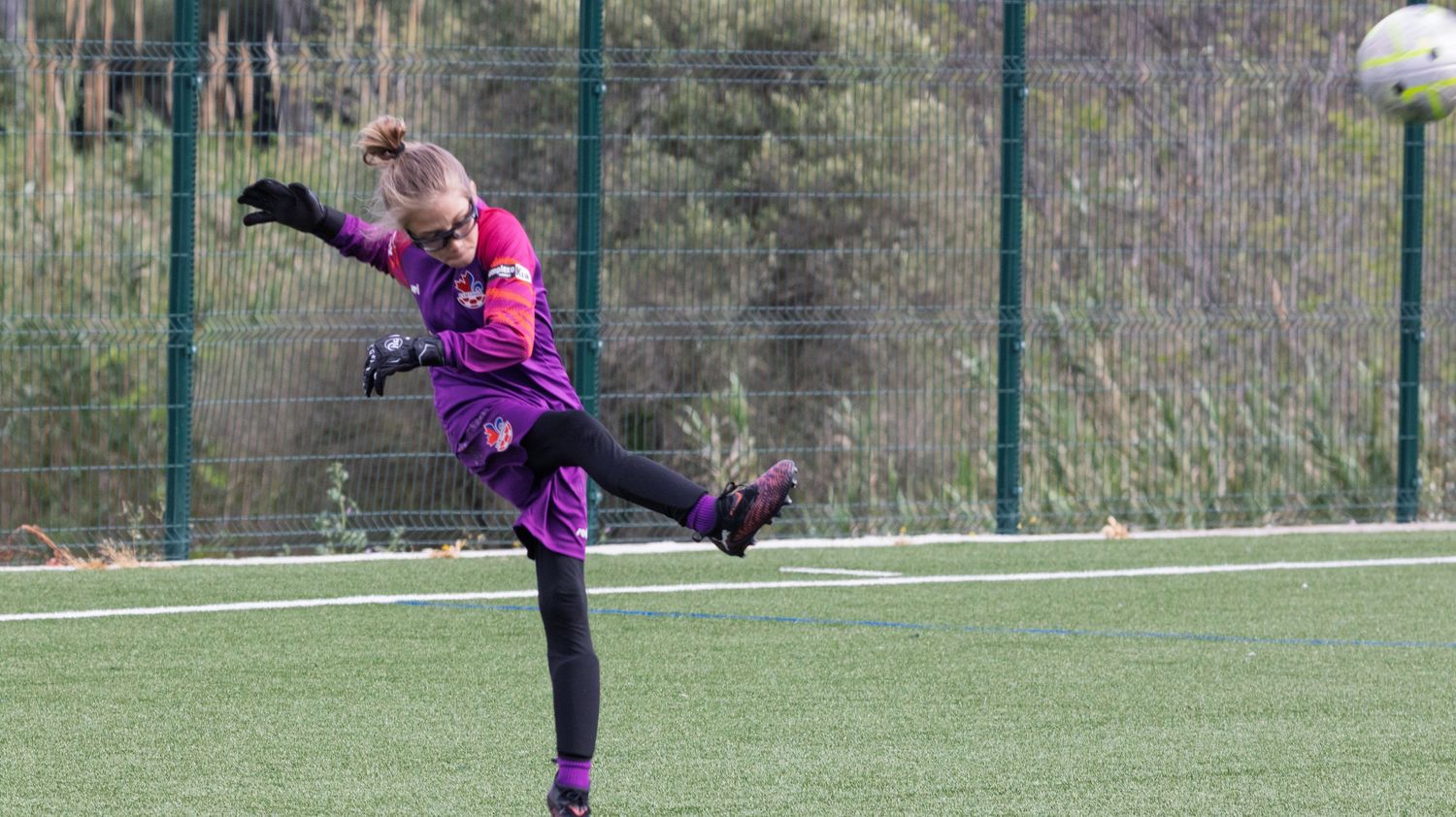 Soccer goalkeeper in purple jersey makes diving save during match.