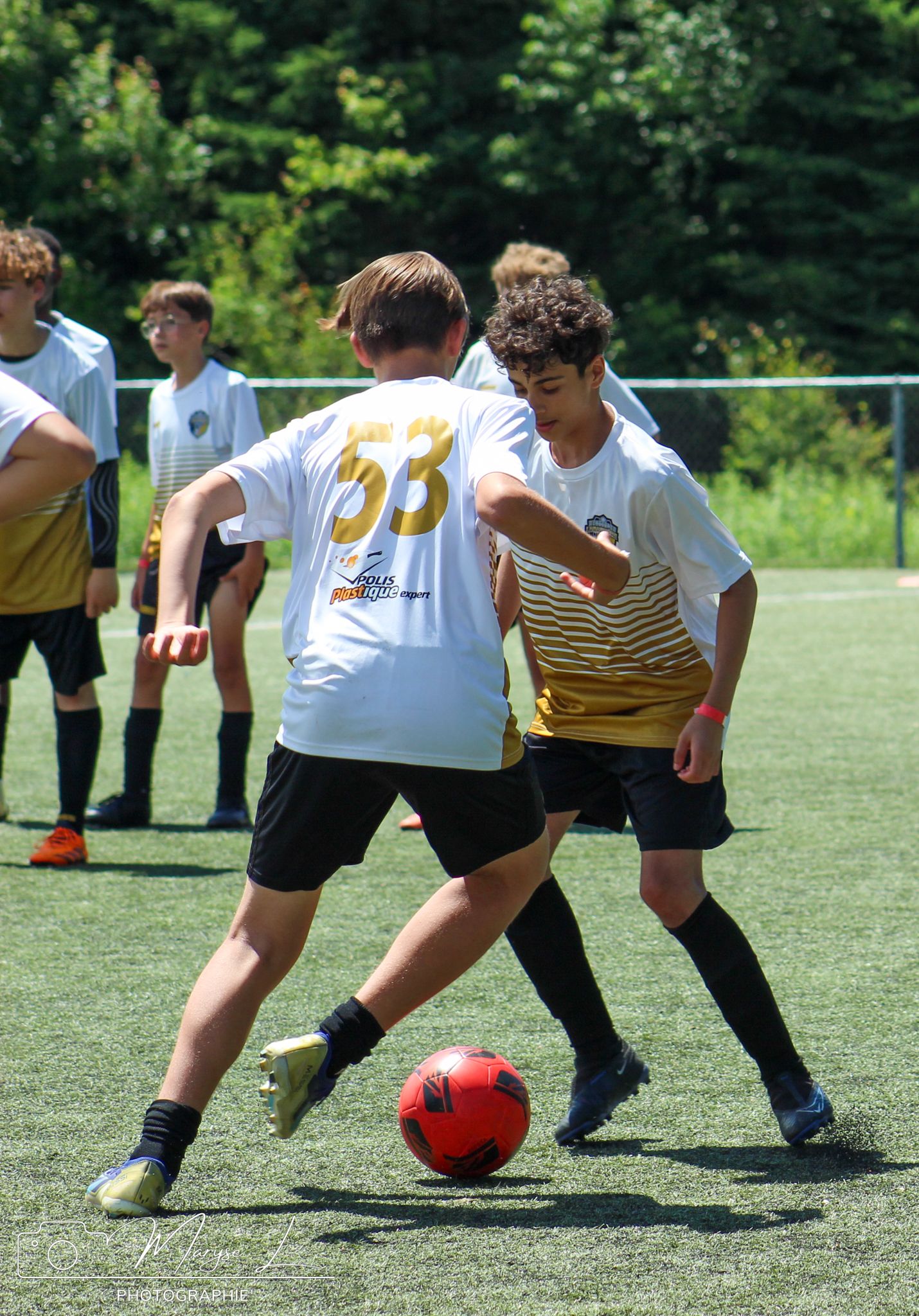 Youth soccer players in white and yellow jerseys competing for the ball during a match.