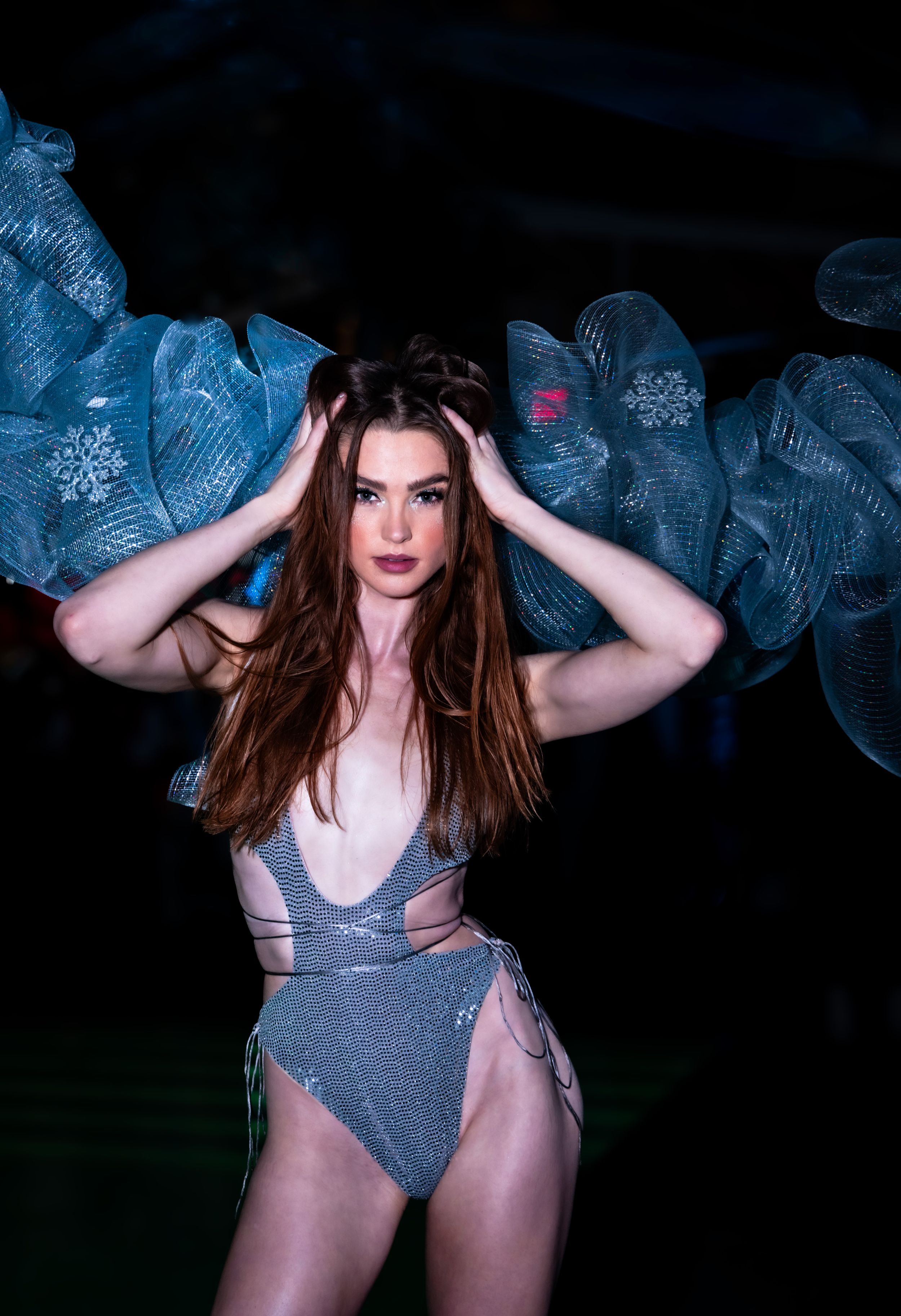 Fashion model in metallic blue swimwear poses dramatically against ethereal blue fabric installation.