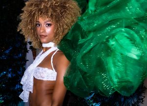 Model in white top with green decorative background during fashion show.