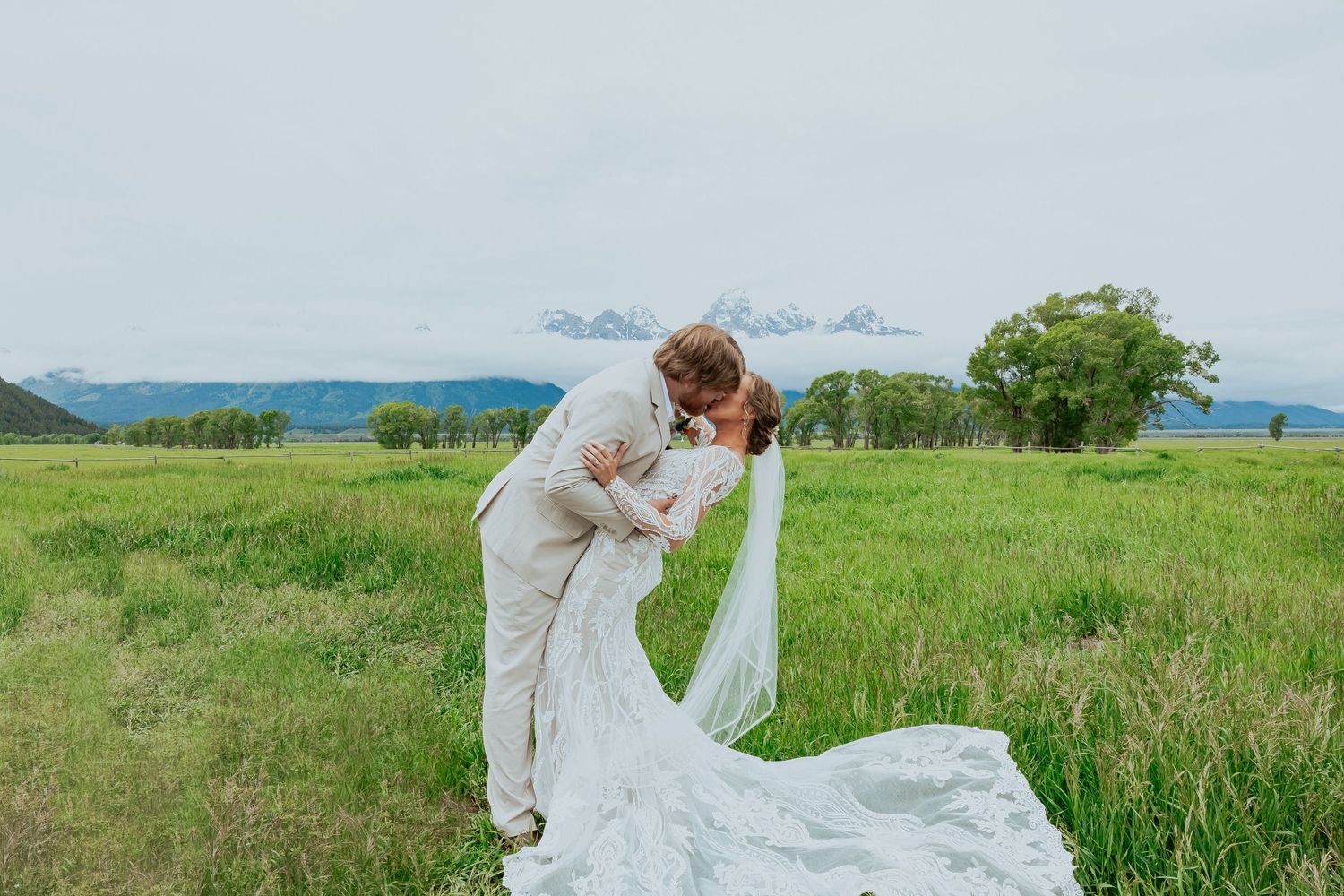 A couple embraces in a romantic moment on a hilltop meadow with mountains in the background.