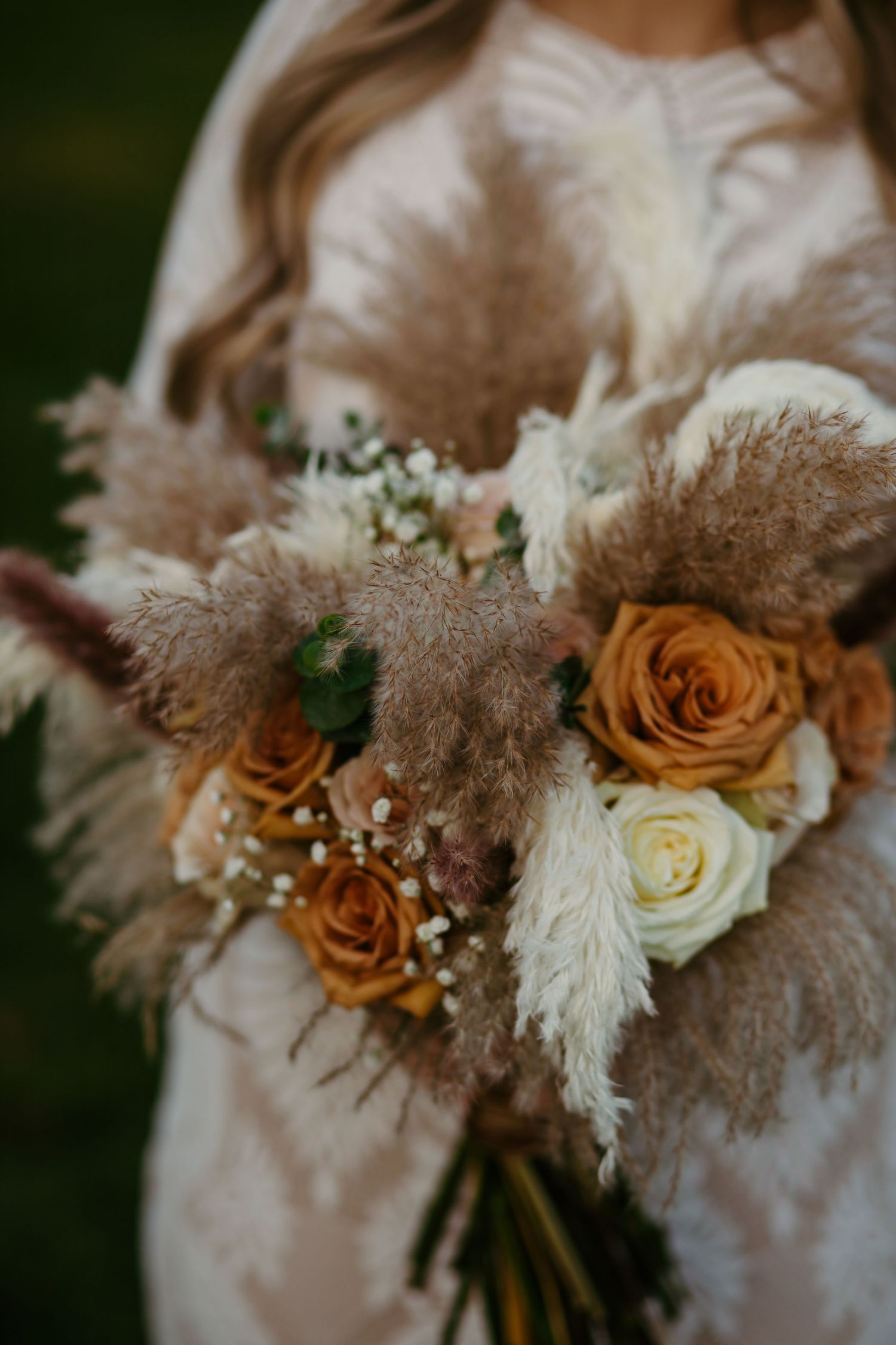 A romantic bridal bouquet featuring orange and white roses with pampas grass and delicate baby's breath.