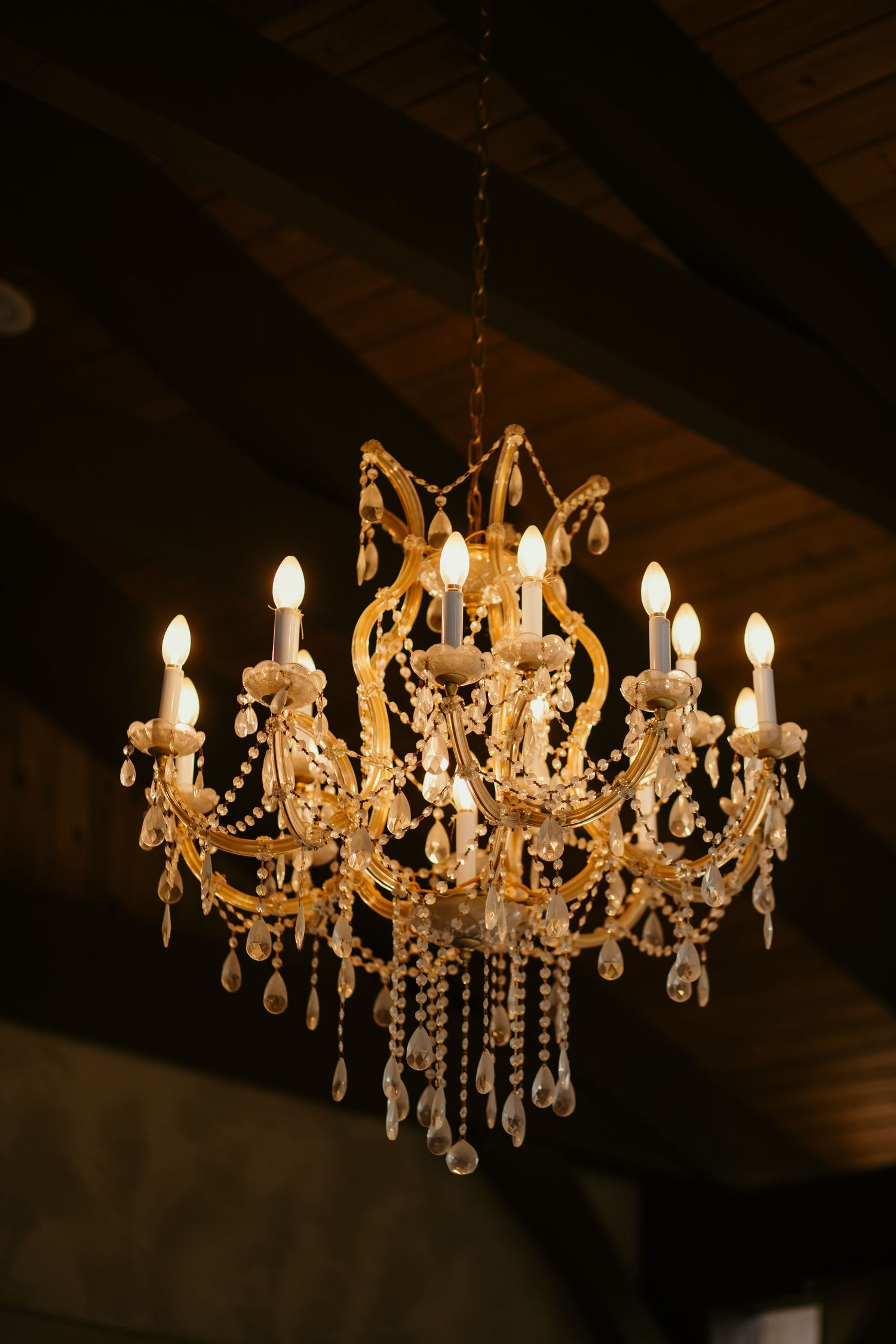 An elegant crystal chandelier with multiple tiers illuminates a dark wooden ceiling.