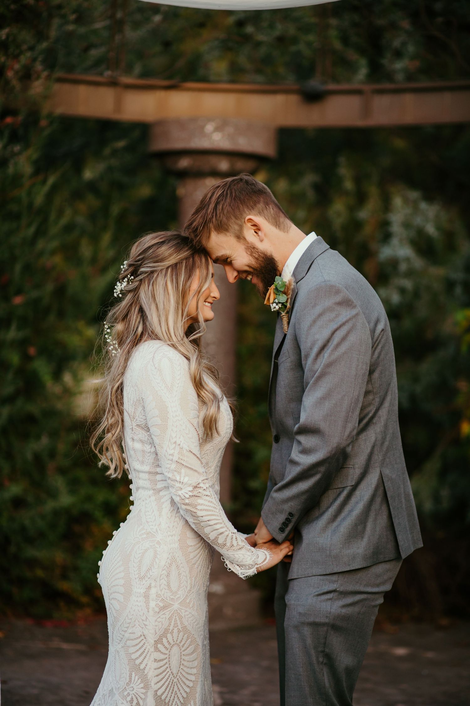 Intimate moment between couple under wooden arch during wedding ceremony.